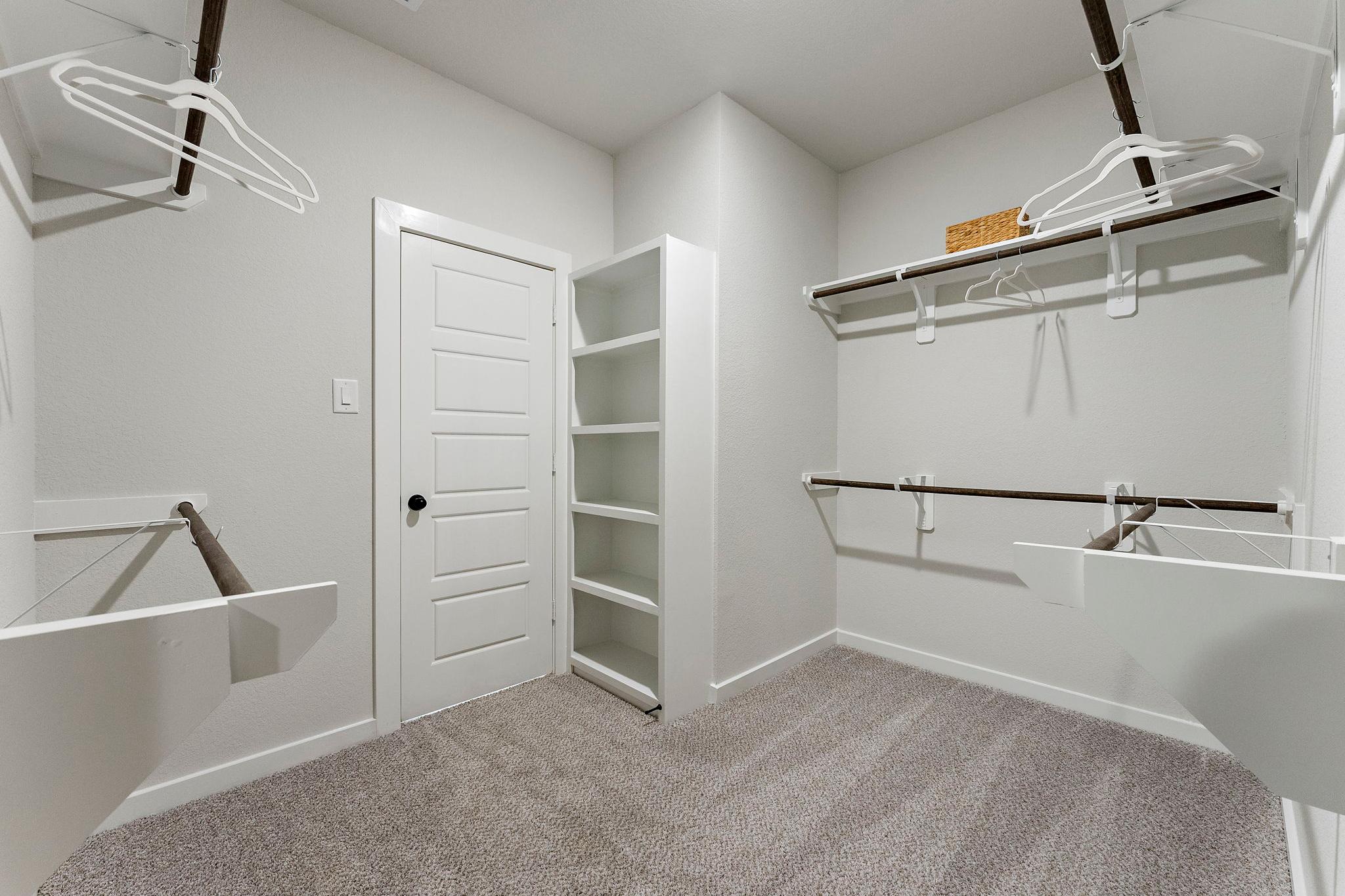 Spacious walk-in closet at Sundance Cove in Crosby Texas by Davidson Homes with built-in shelving, hanging rods and gray carpet
