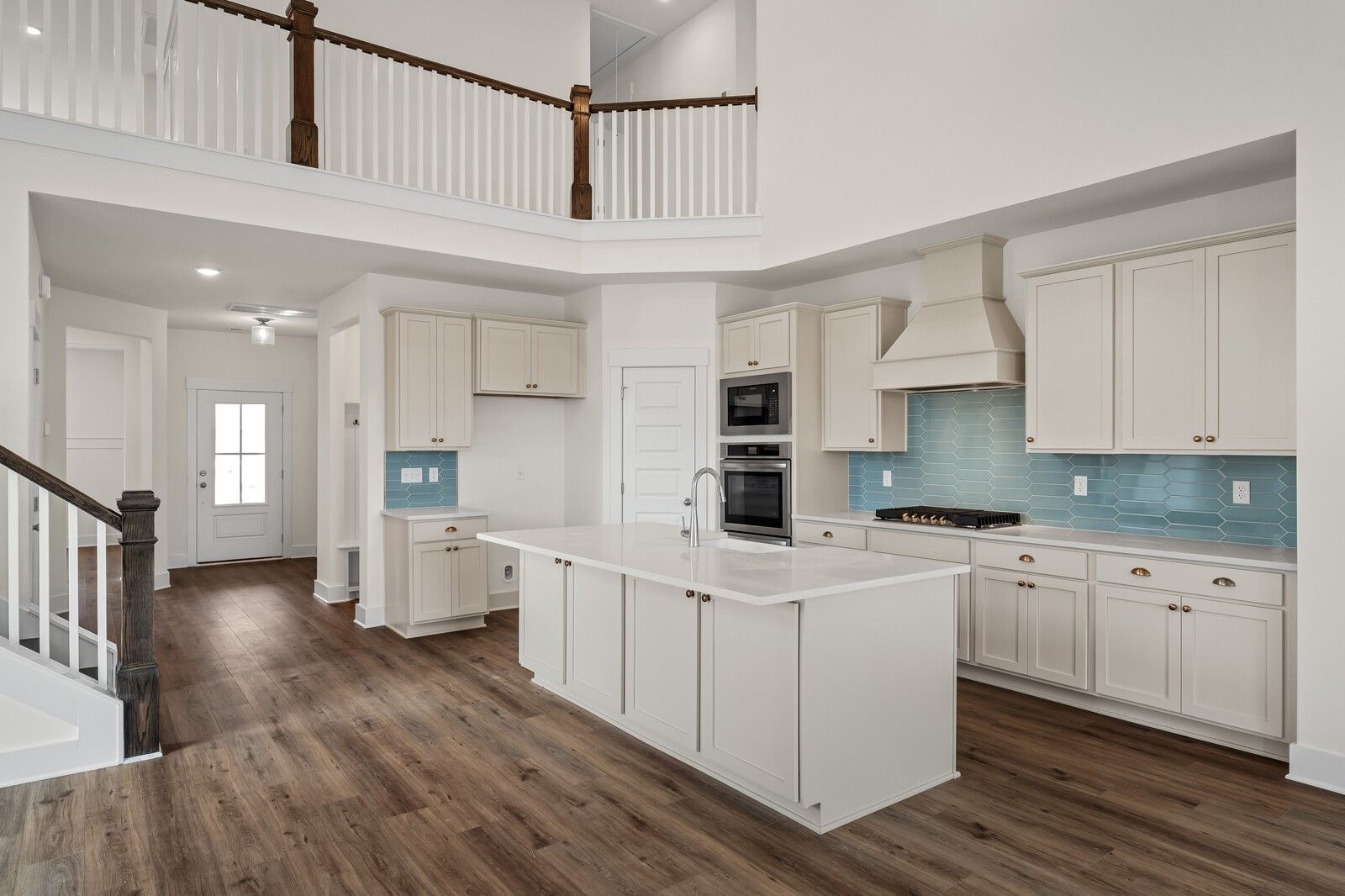 Modern open-concept kitchen with white shaker cabinets, blue tile backsplash, large island, and stainless appliances in 2-story Ridgeport home, Gallatin, TN