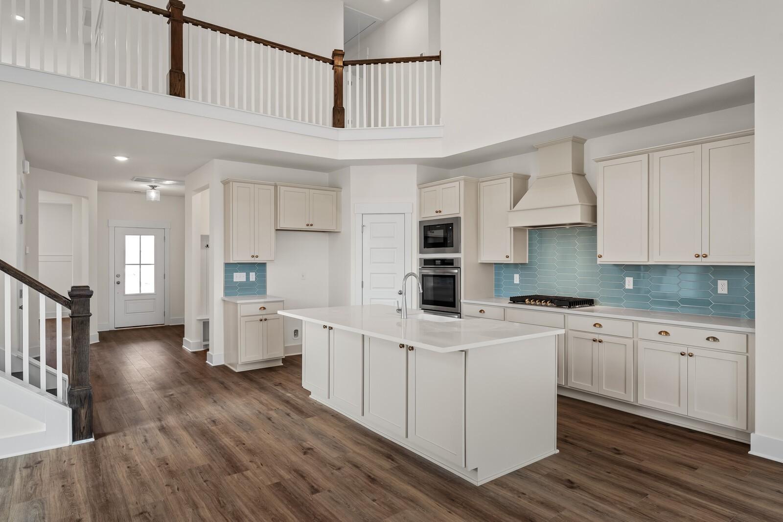 Modern open-concept kitchen with white shaker cabinets, blue tile backsplash, large island, and stainless appliances in 2-story Ridgeport home, Gallatin, TN