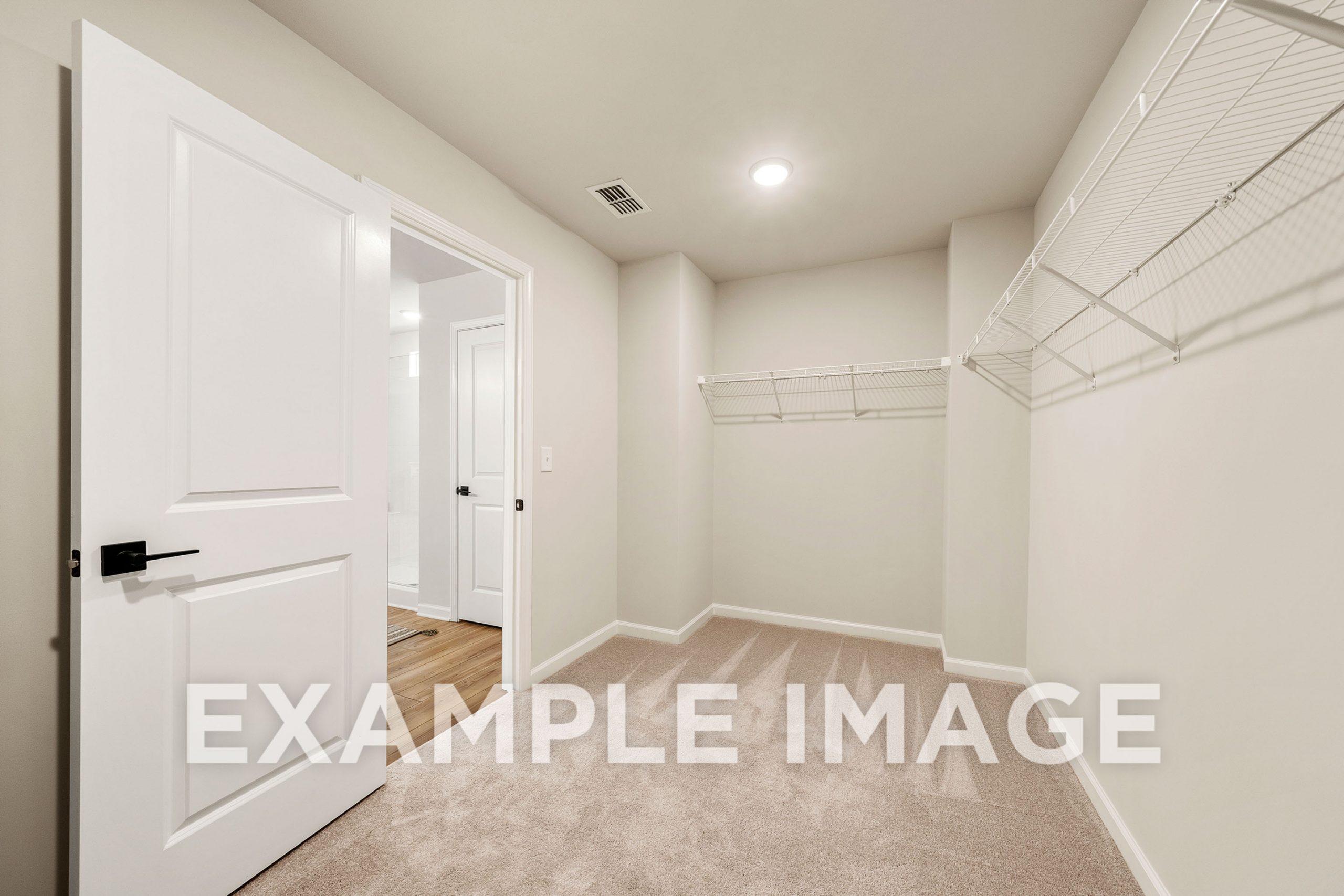 Spacious walk-in closet in The Hickory B master suite featuring wire shelving, beige walls, and carpeted floor