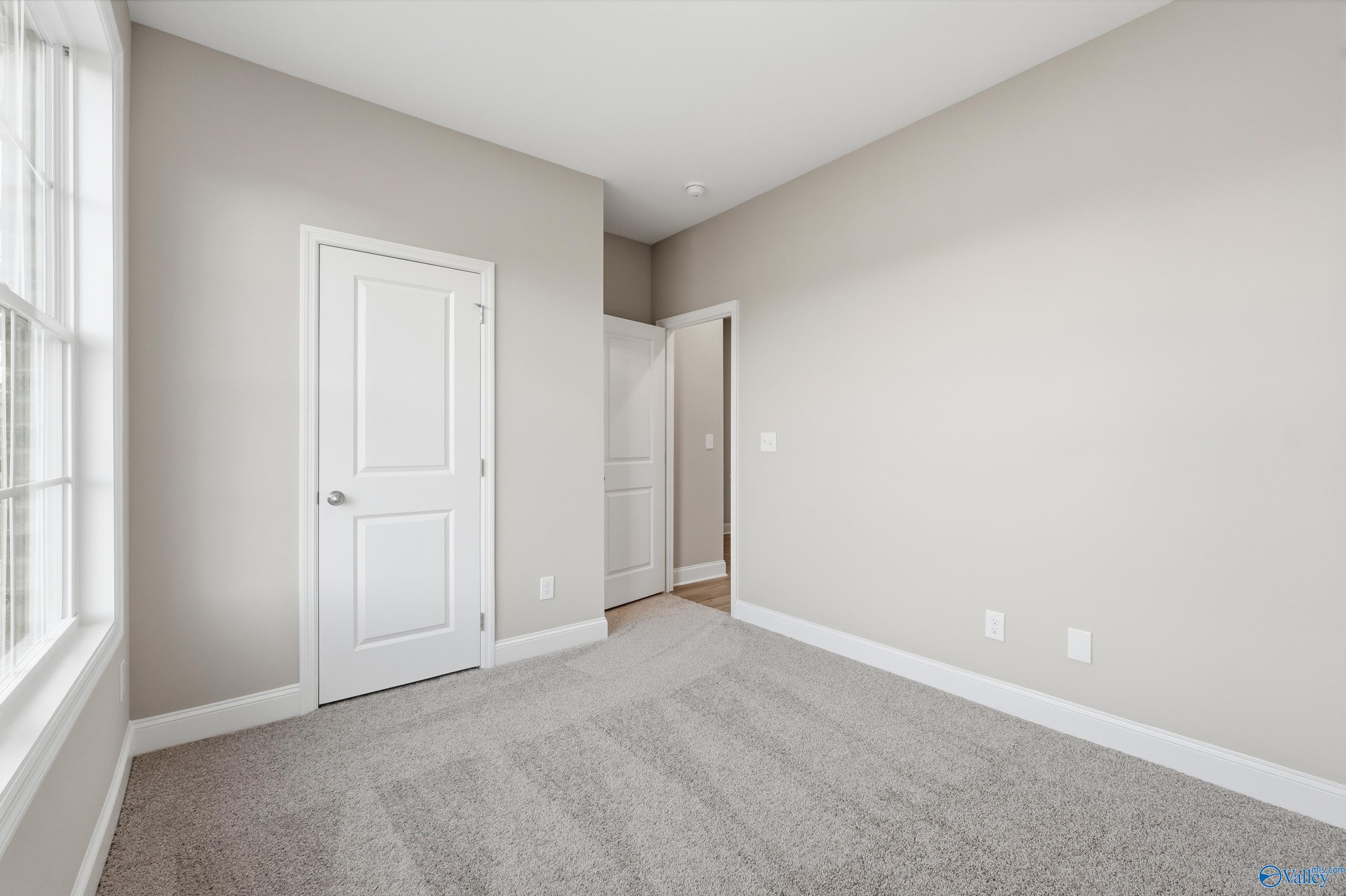 Bright empty bedroom with large window, neutral walls, and carpet floor in Davidson Homes The Asheville, Arab Alabama
