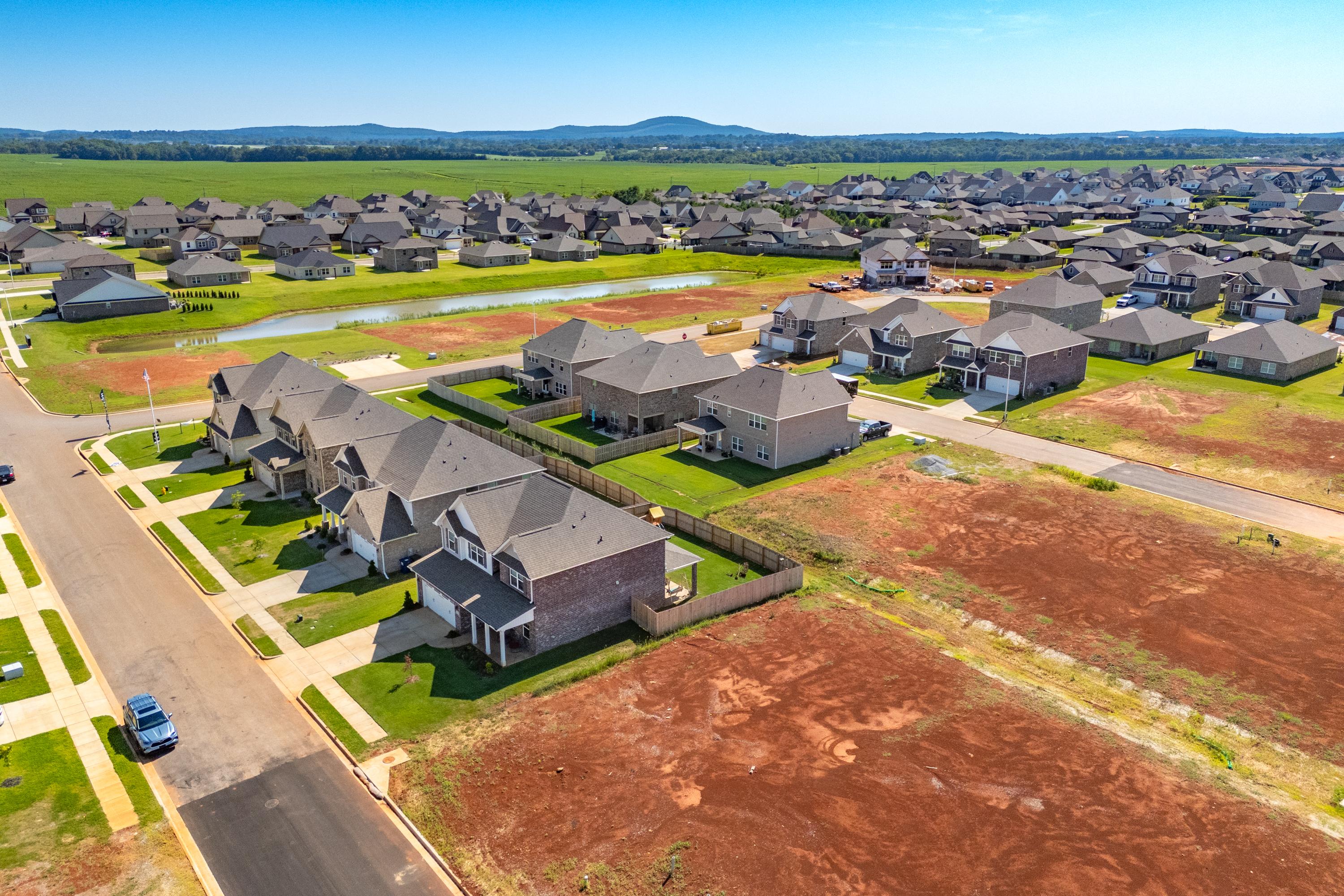 Aerial view of Walker's Hill neighborhood in Meridianville AL with new Davidson Homes, pond, green fields and red clay lots