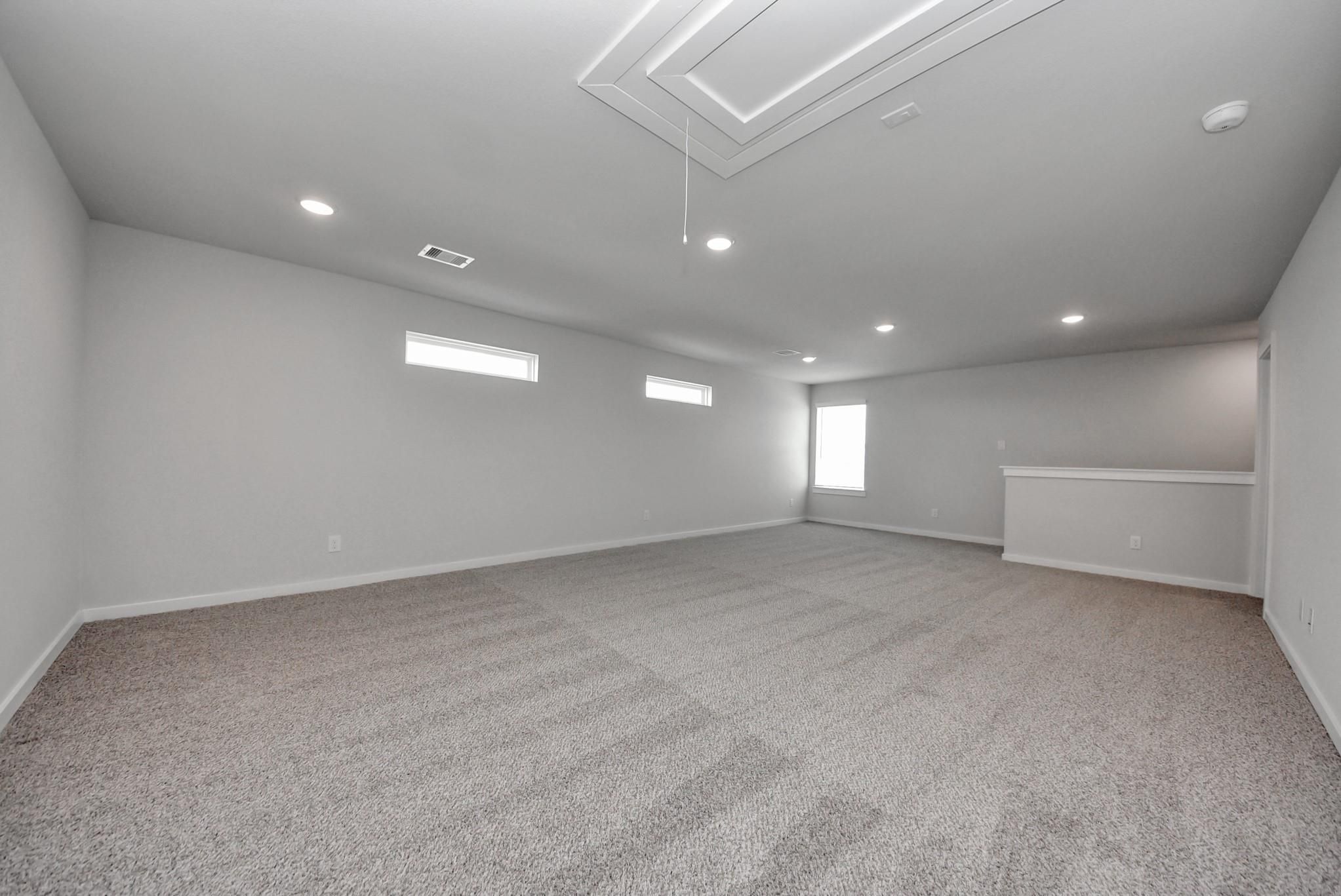 Spacious upstairs game room with tray ceiling, carpet flooring, and clerestory windows in Davidson Homes The San Marcos E, Beasley, TX