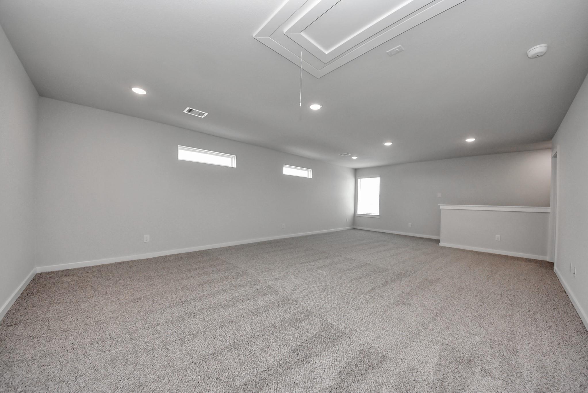 Spacious upstairs game room with tray ceiling, carpet flooring, and clerestory windows in Davidson Homes The San Marcos E, Beasley, TX