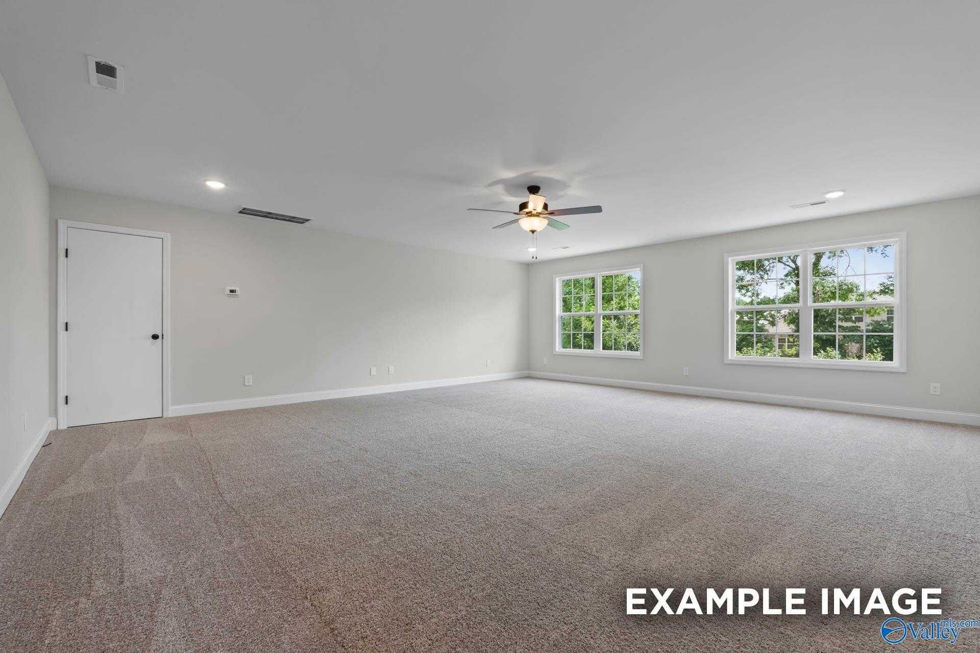 Bright secondary bedroom with large windows overlooking trees, ceiling fan, neutral walls and carpet in The Kirkland home, Decatur, Alabama