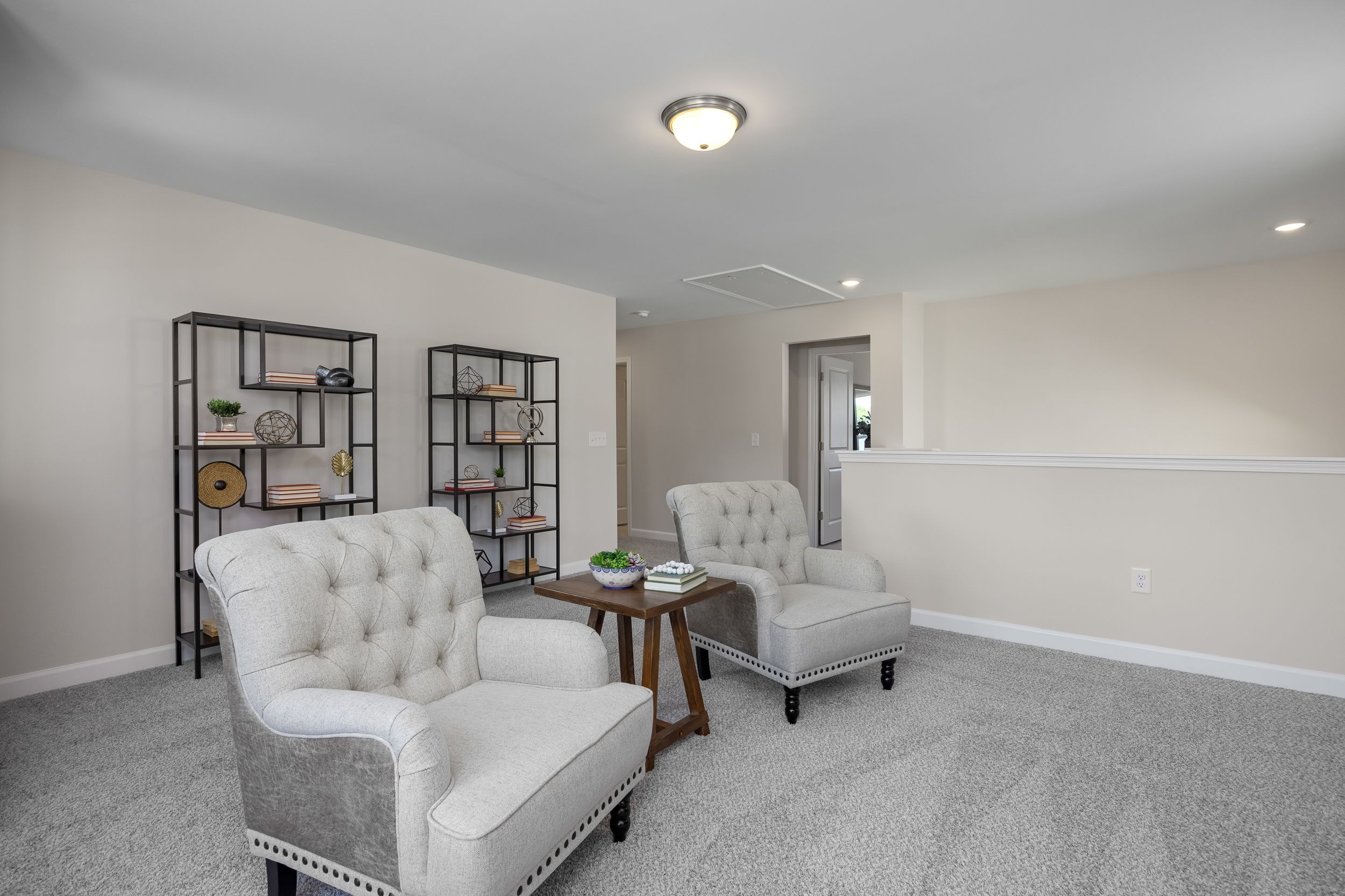 Cozy seating nook in Montrose Aberdeen NC home by Davidson Homes with tufted cream armchairs, wooden table, and metal bookshelves