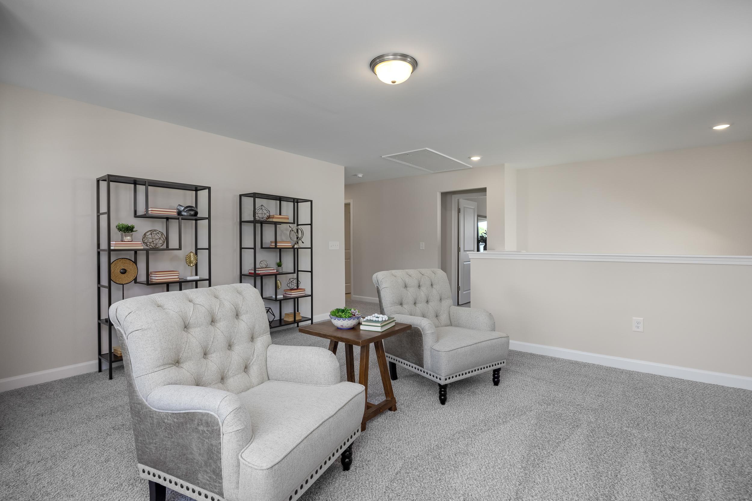 Cozy seating nook in Montrose Aberdeen NC home by Davidson Homes with tufted cream armchairs, wooden table, and metal bookshelves