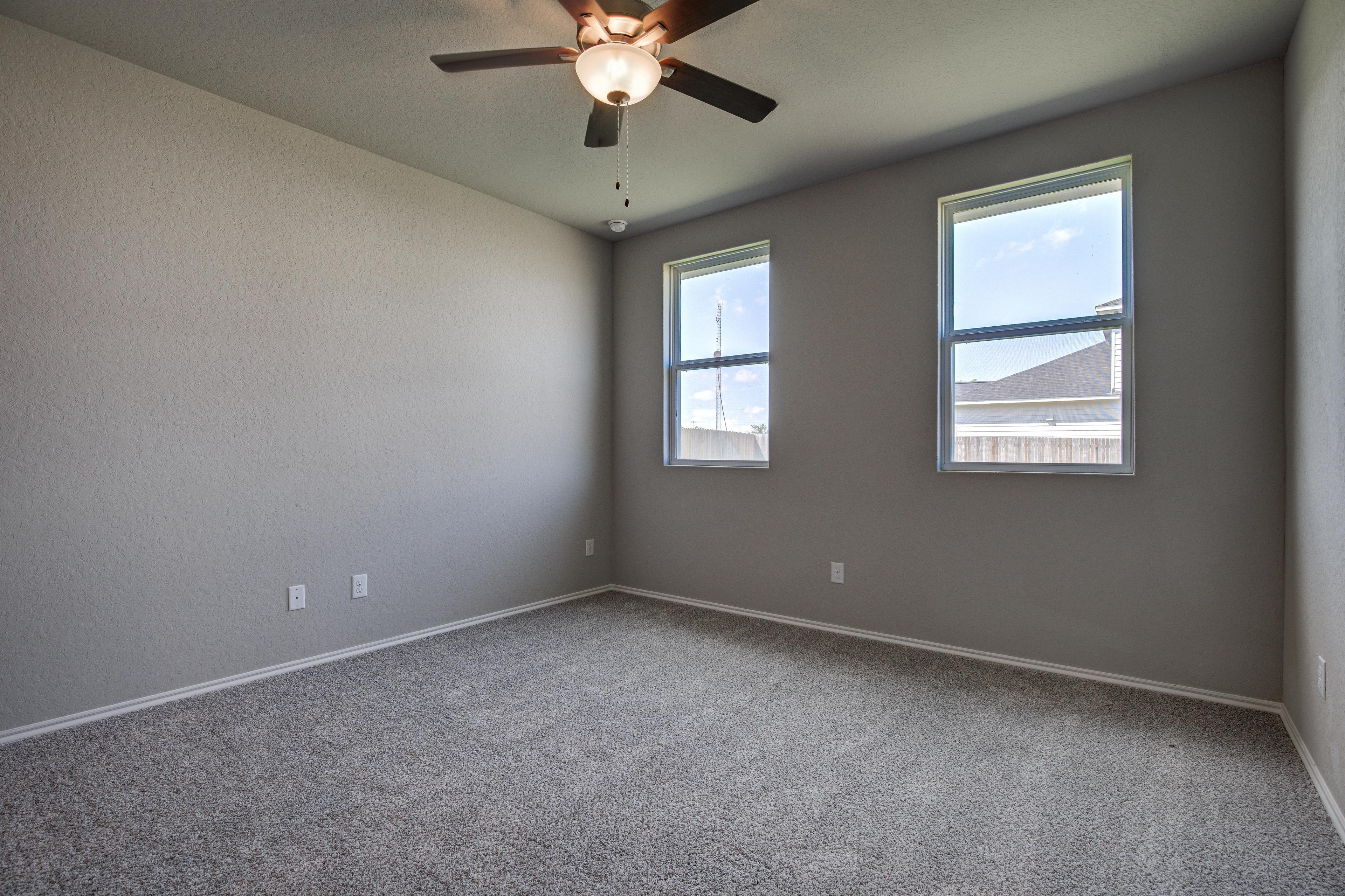 Spacious empty bedroom in The Asheville with gray walls, carpet flooring, large double windows, and ceiling fan