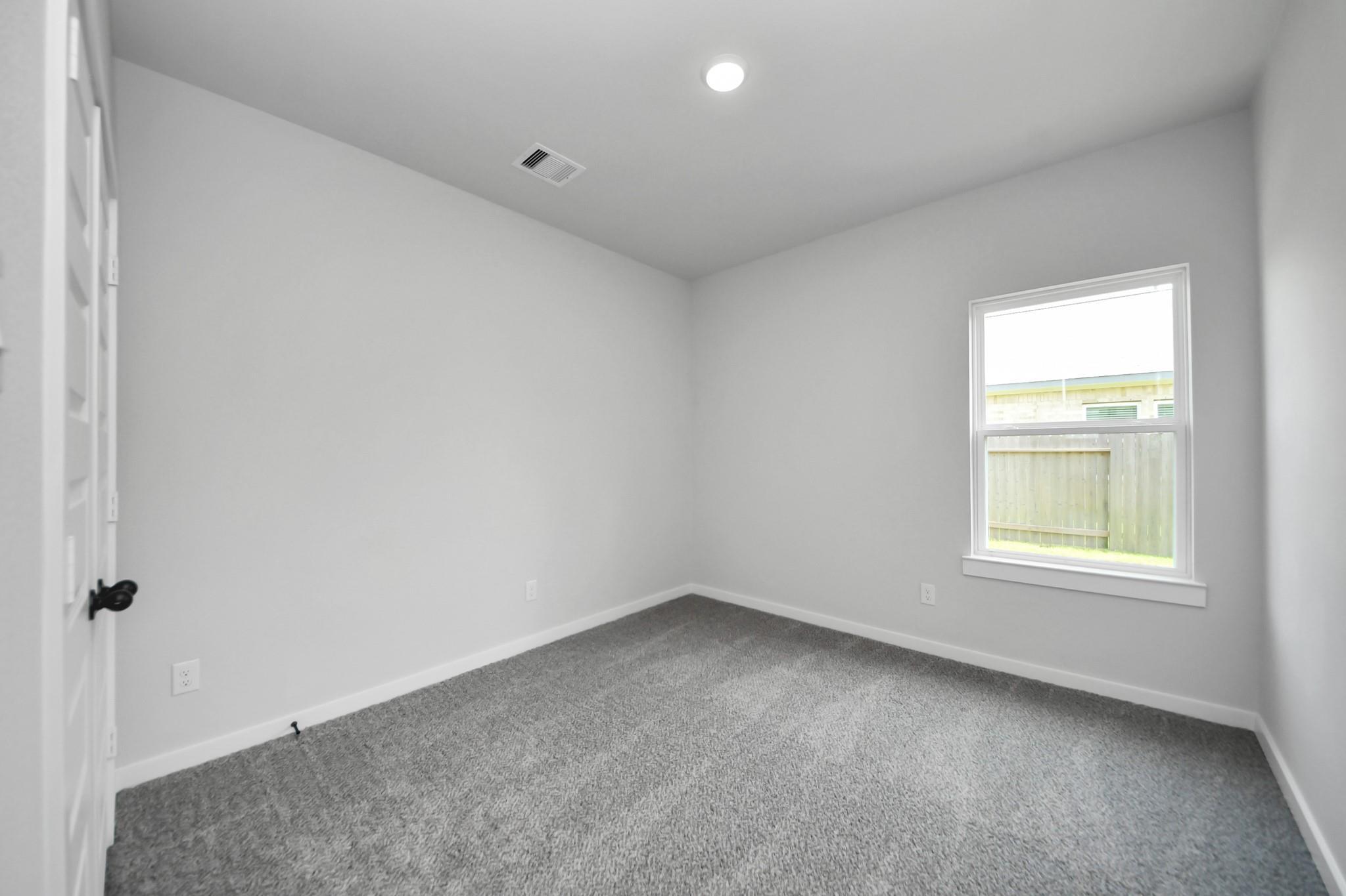 Bright, spacious secondary bedroom with plush carpeting in The Riviera C floor plan at River Ranch Meadows, Dayton, Texas.