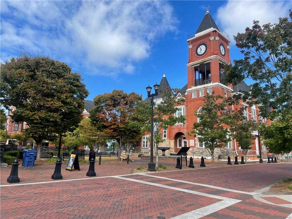 Historic red brick courthouse with clock tower, autumn trees, and brick plaza under blue sky in Dallas, Georgia
