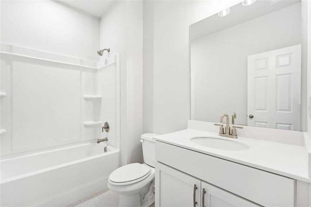 Bright white secondary bathroom with tub-shower combo, single vanity, and mirror in The Hickory C by Davidson Homes, Hoschton, GA