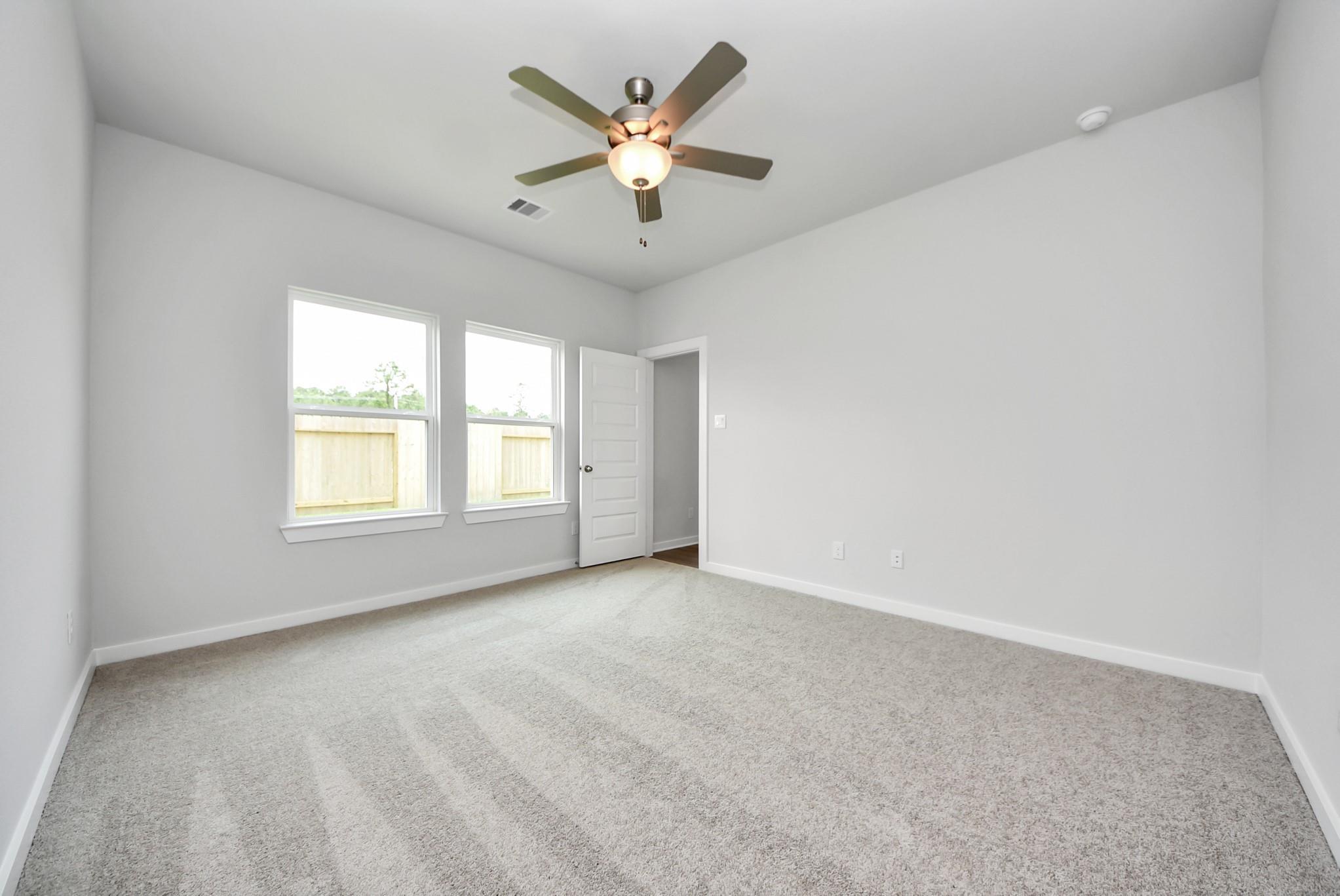 Spacious carpeted bedroom with ceiling fan in The Blanco E floor plan at The Villages at WestPointe in Dayton, Texas.