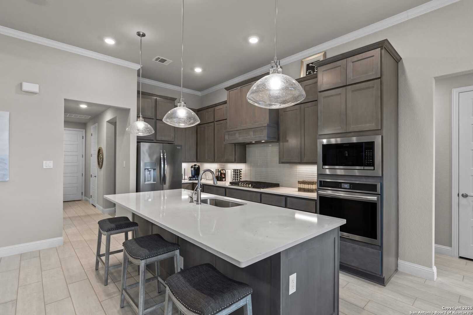 Modern kitchen with quartz island, stainless steel appliances, pendant lights, and bar stools in Davidson Homes The Garner B, Castroville, TX