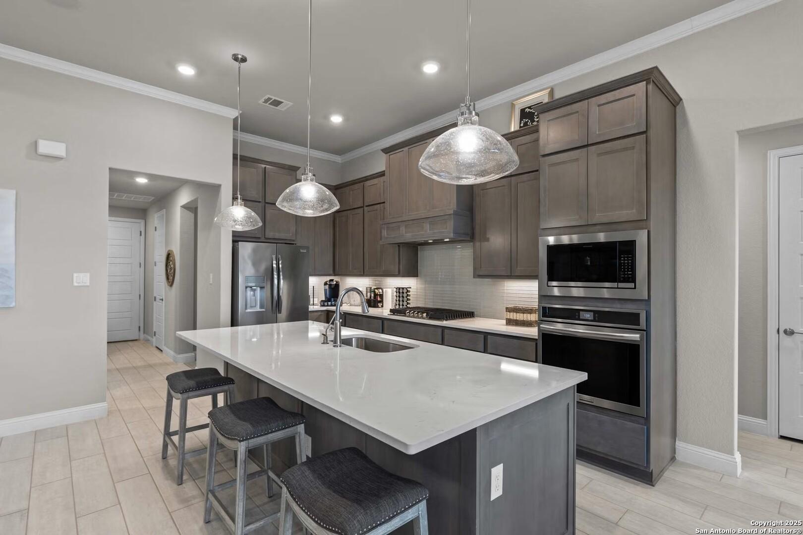Modern kitchen with quartz island, stainless steel appliances, pendant lights, and bar stools in Davidson Homes The Garner B, Castroville, TX