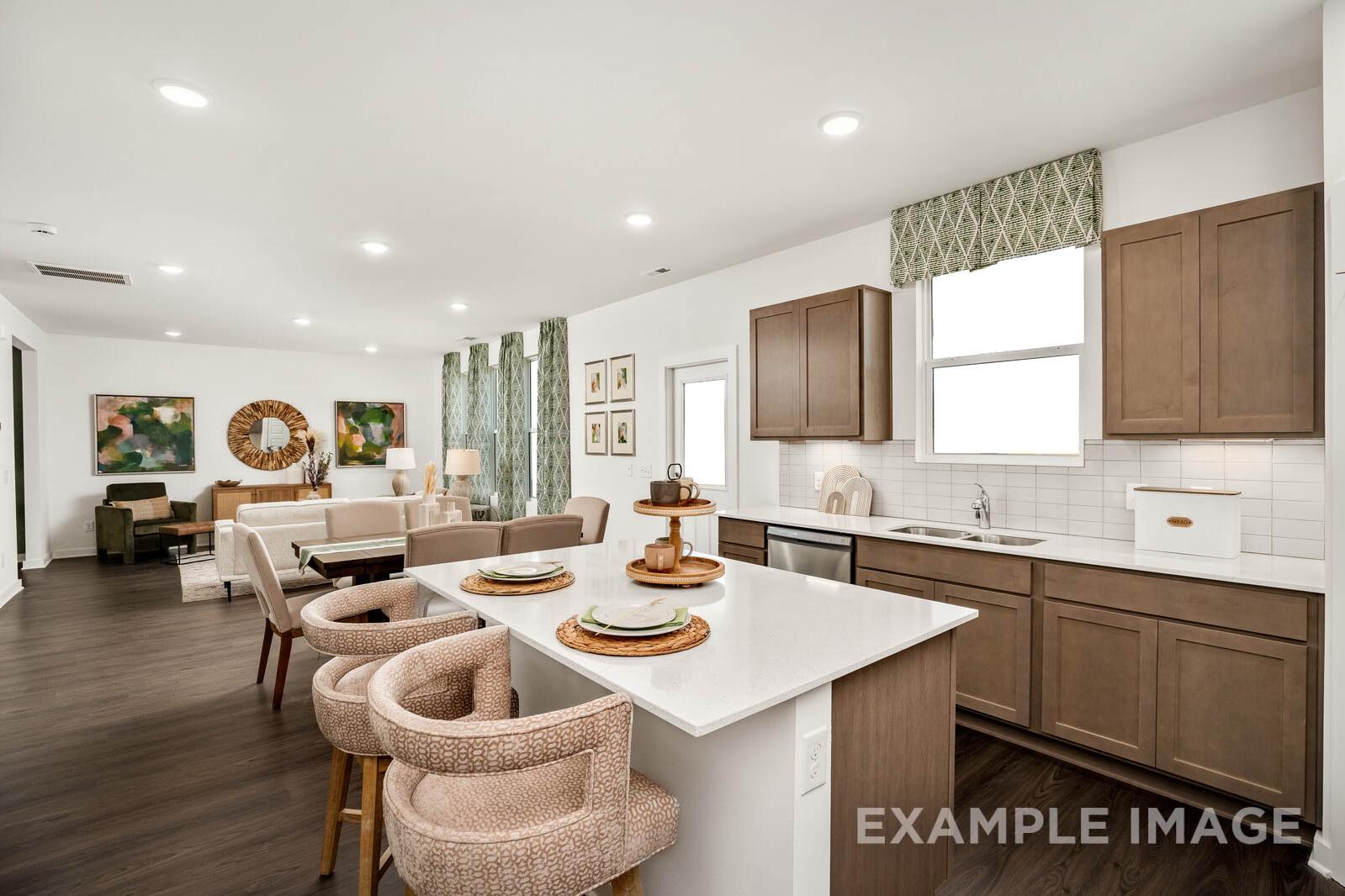Open-concept kitchen and living space in The Gordon C with white island, wood cabinets, upholstered stools, and beige sofa