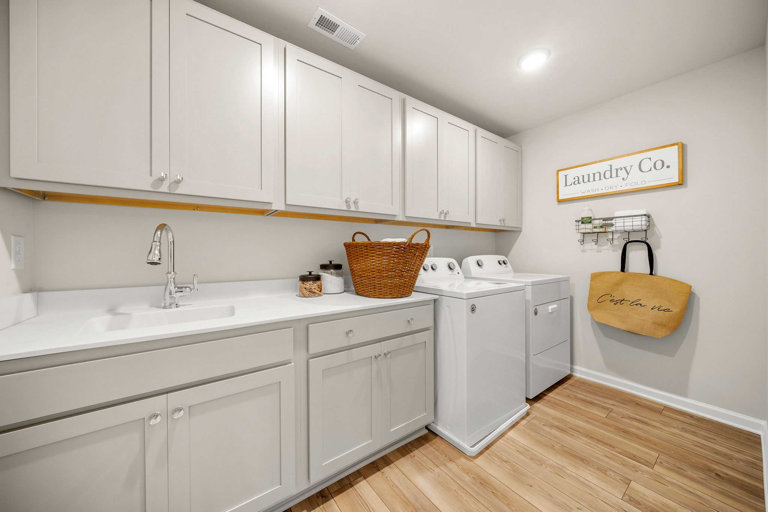 Laundry room in Riverwood, Dallas, GA by Davidson Homes with white cabinets, utility sink, washer, dryer, hardwood floors