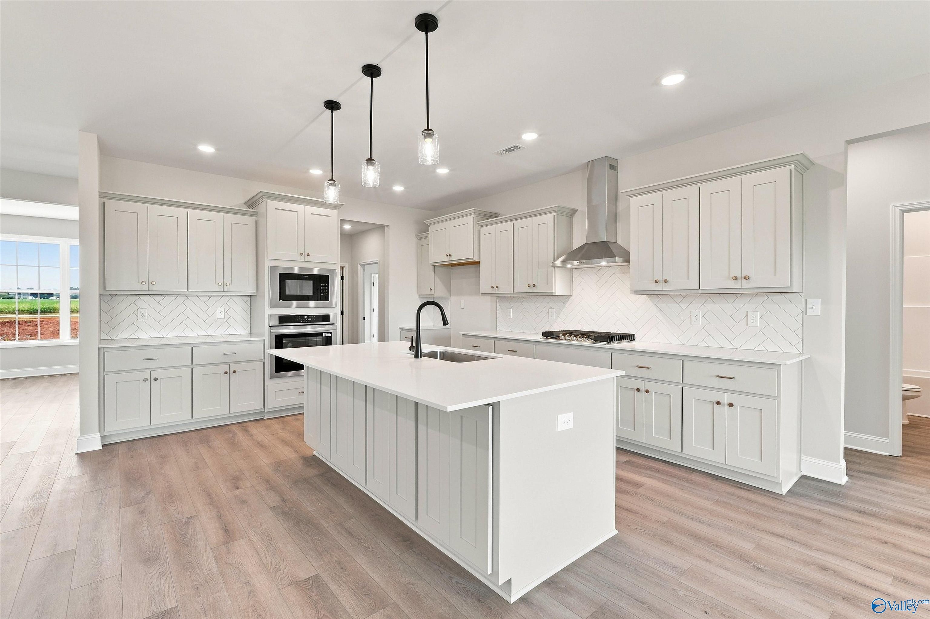 Modern kitchen with white island, herringbone backsplash, and stainless appliances in The Oxford floor plan, Kendall Farms.