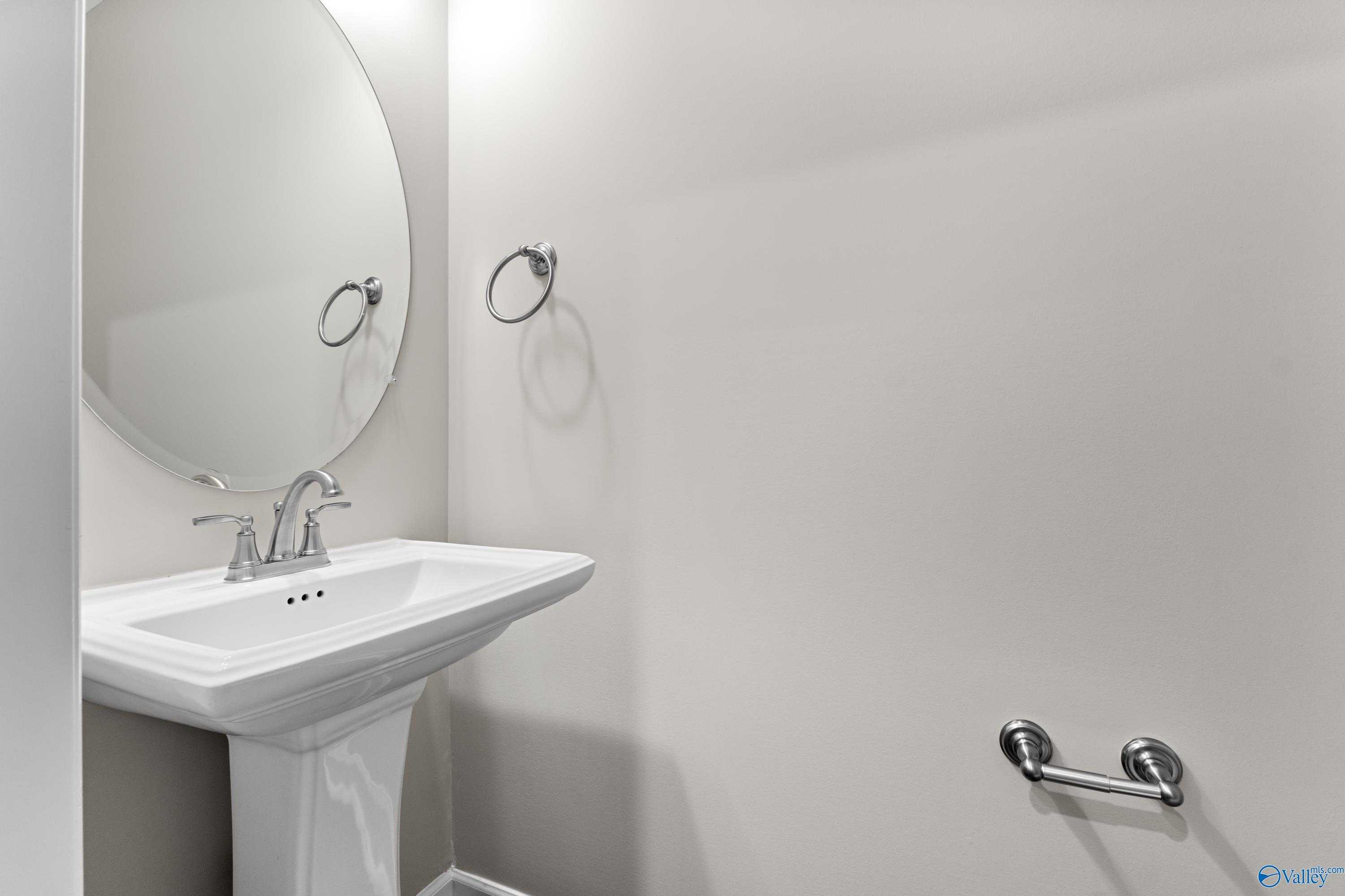 Elegant powder room with white pedestal sink, round mirror, chrome fixtures in Davidson Homes The Haven, Huntsville AL