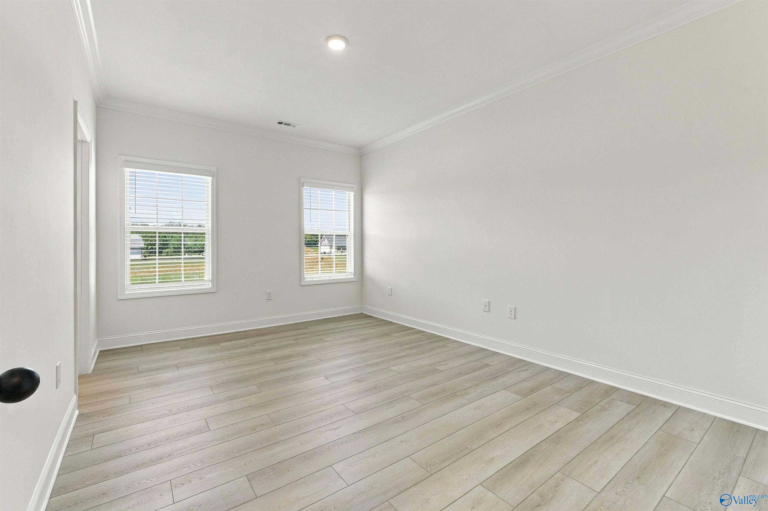 Bright empty bedroom with light wood flooring, white walls, and two windows in Davidson Homes The Valencia, Huntsville, Alabama