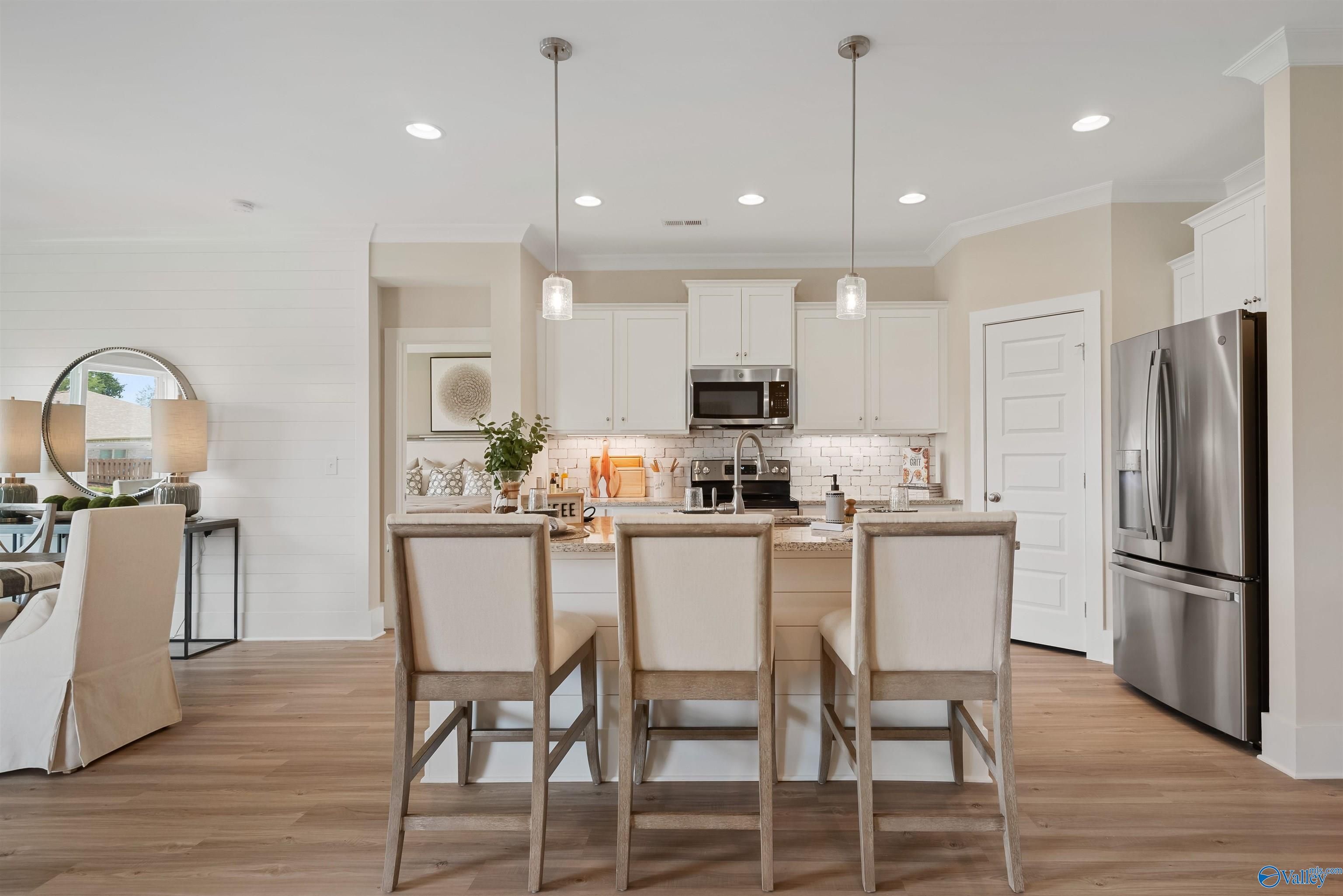 Modern open-concept kitchen with white shaker cabinets, stainless steel appliances, and wood island bar stools in Davidson Homes The Everett, New Market, AL