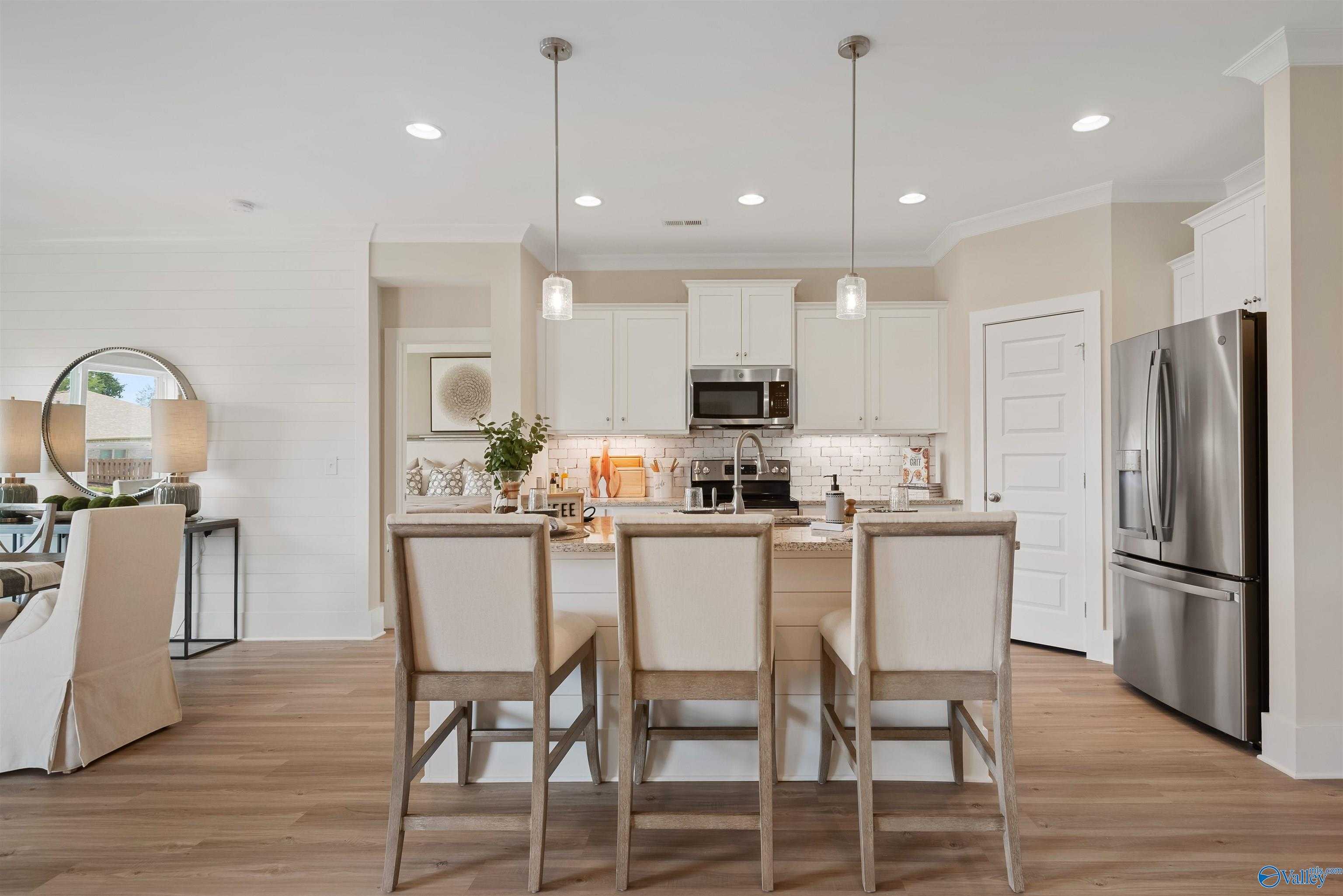 Modern open-concept kitchen with white shaker cabinets, stainless steel appliances, and wood island bar stools in Davidson Homes The Everett, New Market, AL