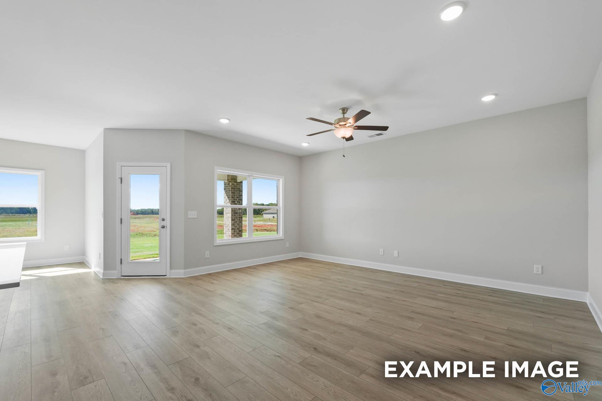 Spacious living room with light wood floors and ceiling fan in The Everett B floor plan at The Meadows, Athens, Alabama.
