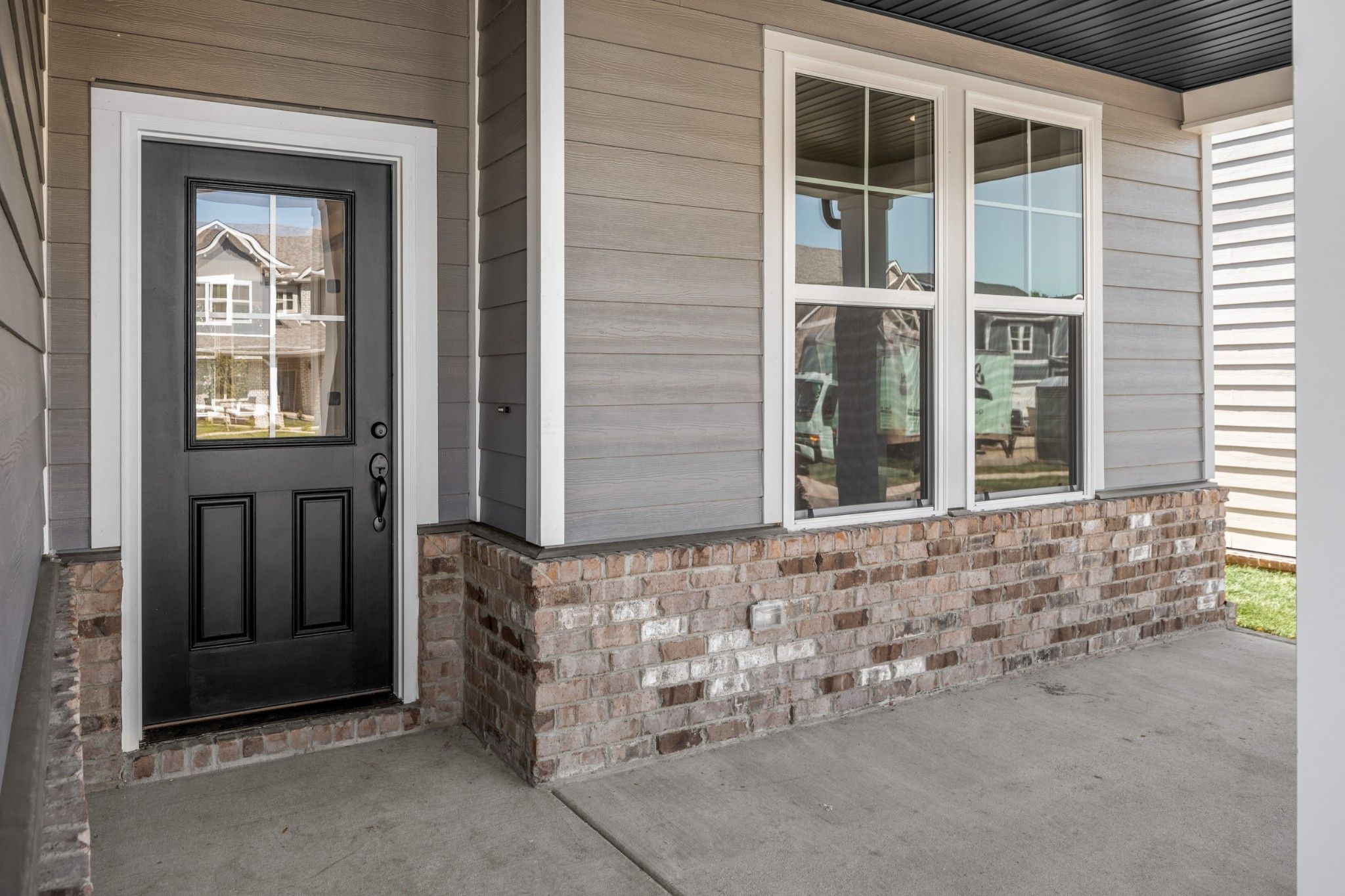 Modern front entrance of The Henry C 4-bedroom home featuring black double door, large windows, gray siding, and brick accents in Calista Farms, White House, Tennessee