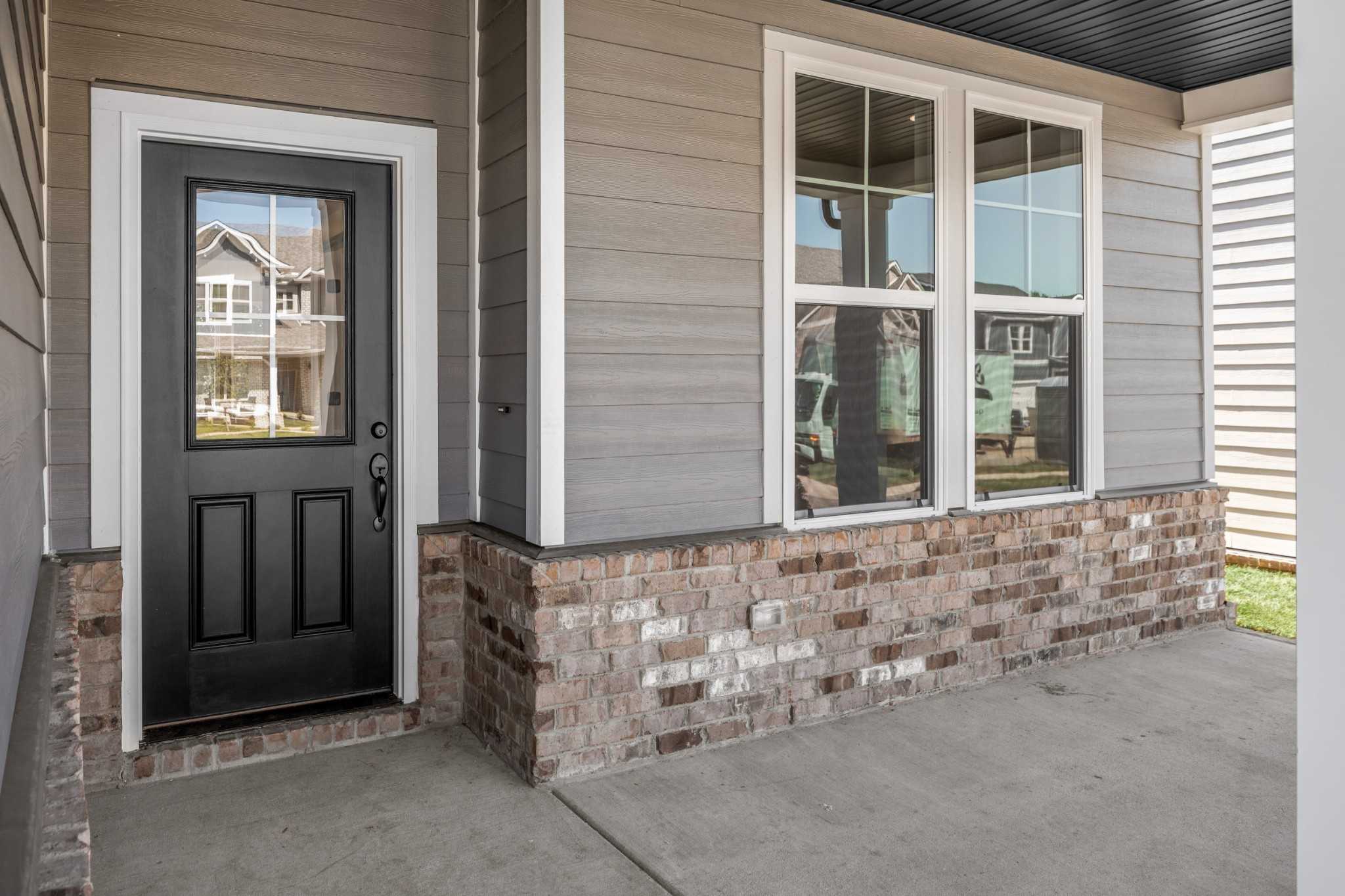 Modern front entrance of The Henry C 4-bedroom home featuring black double door, large windows, gray siding, and brick accents in Calista Farms, White House, Tennessee