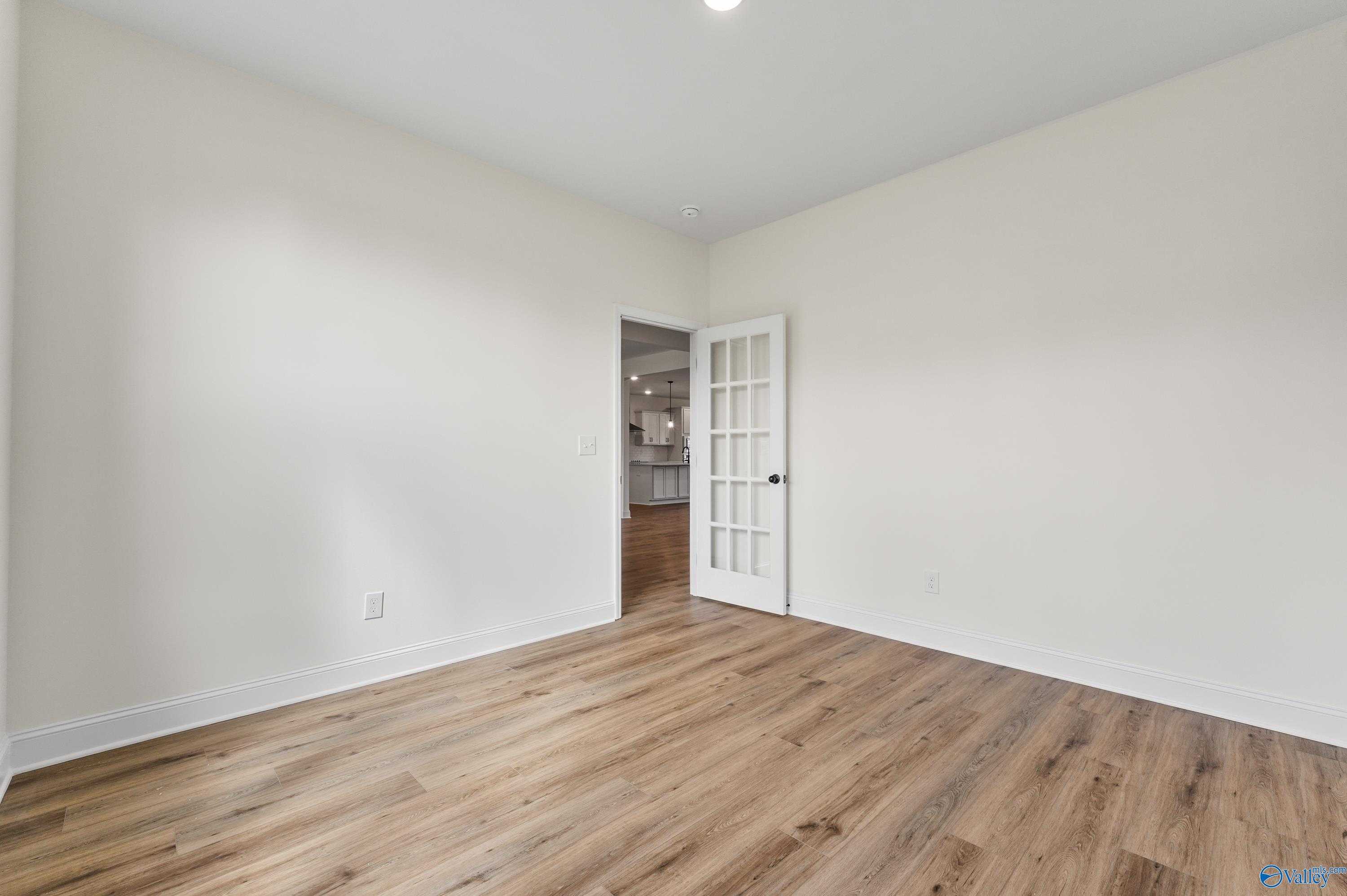 Bright bedroom featuring light oak floors, white walls, and French door to laundry area in Davidson Homes The Finleigh, Harvest AL