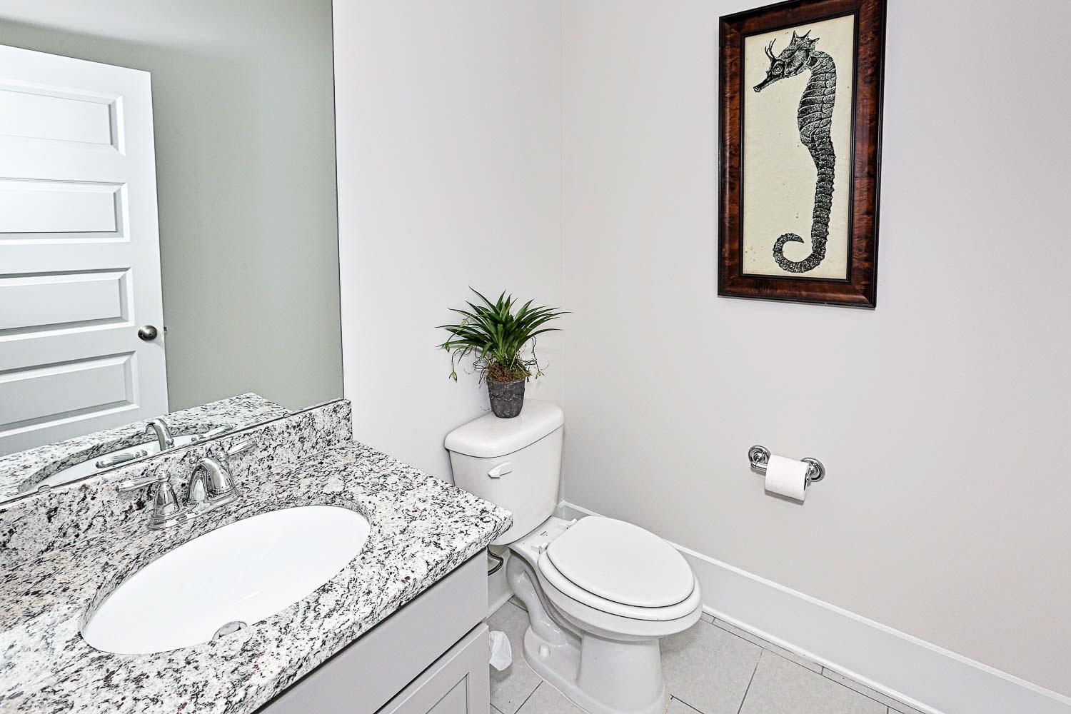 Modern powder room in The Finleigh featuring granite vanity, white sink, toilet, seahorse artwork, and potted plant