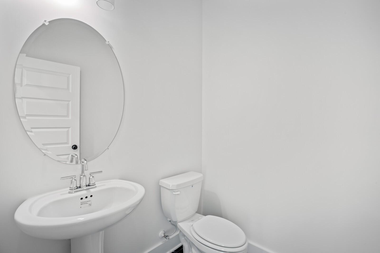 Bright white powder room with large round mirror, pedestal sink and toilet in Davidson Homes The Willow, Gallatin, Tennessee