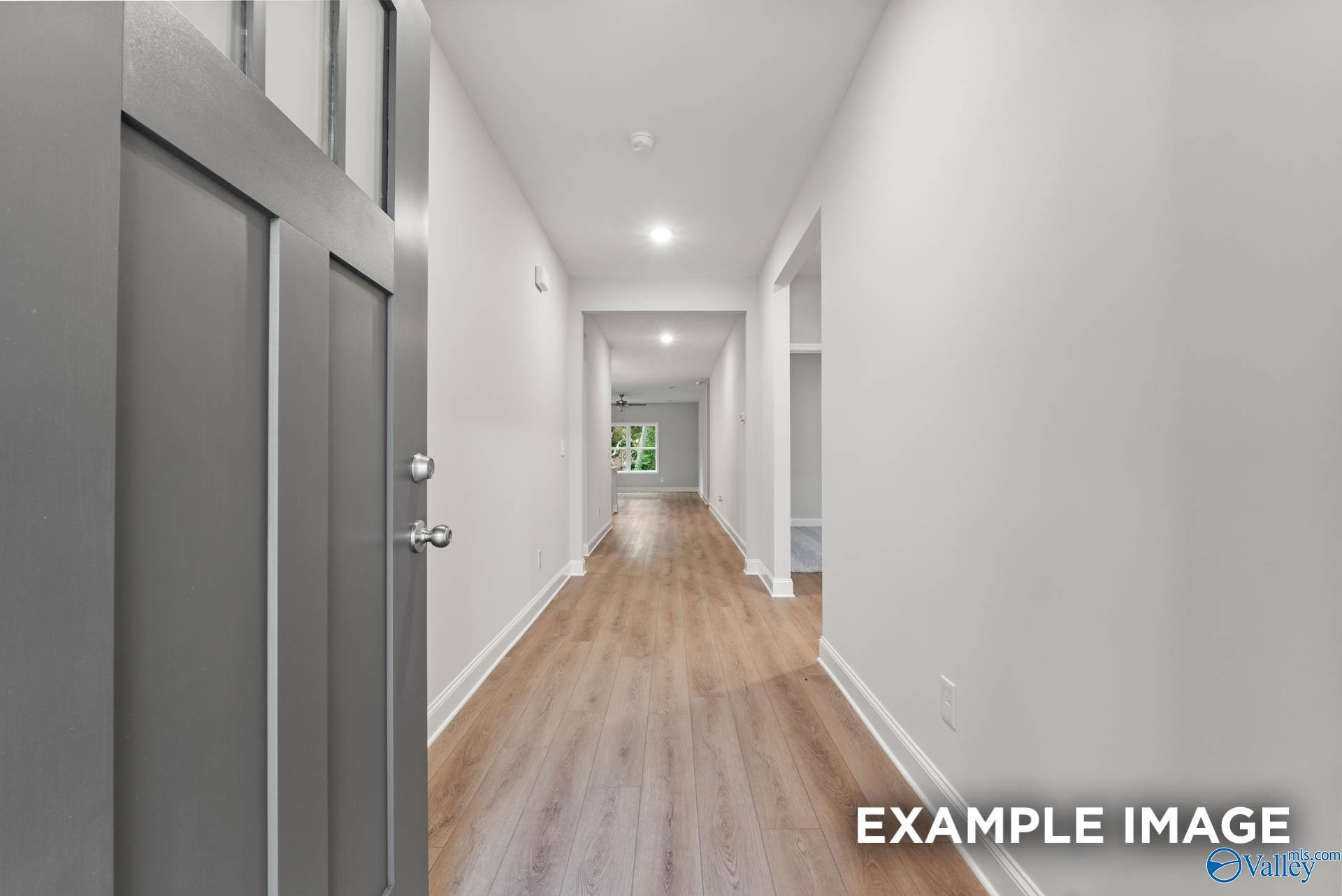 Inviting entry hallway with open gray front door, hardwood floors, and white walls in Davidson Homes The Daphne, Meridianville, Alabama