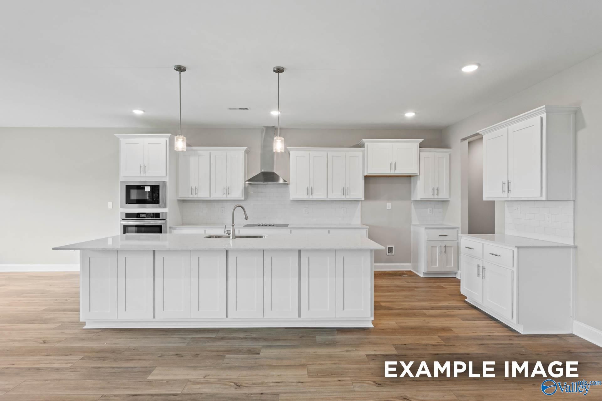 Modern white kitchen featuring large island, pendant lights, and hardwood floors in The Finleigh home by Davidson Homes, Harvest, AL