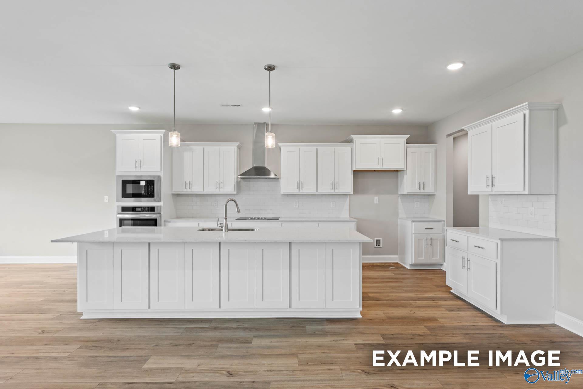 Modern white kitchen featuring large island, pendant lights, and hardwood floors in The Finleigh home by Davidson Homes, Harvest, AL