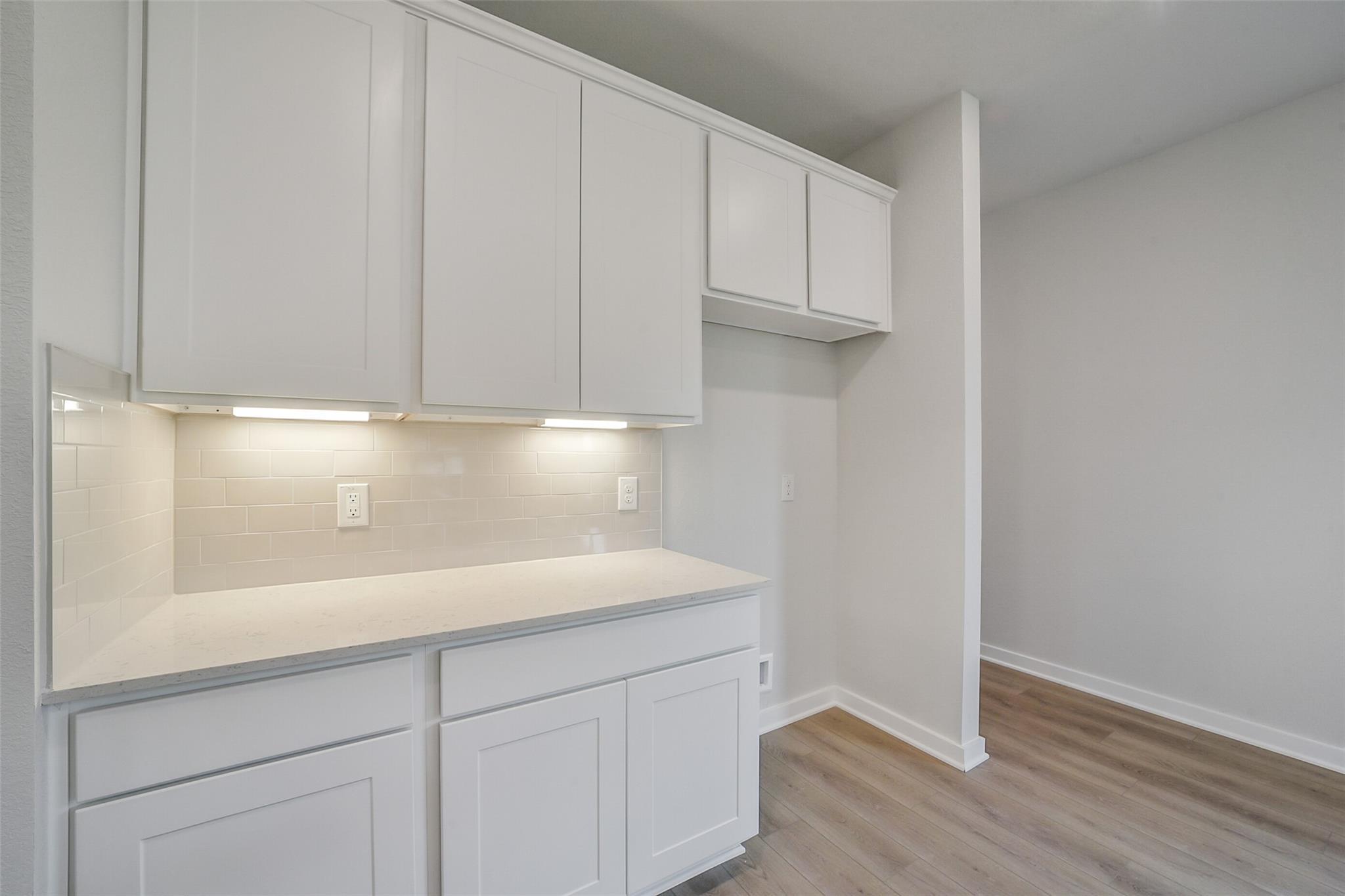 White shaker kitchen cabinets with quartz counters, subway tile backsplash, and under-cabinet lighting in Davidson Homes The Frio F, Conroe, Texas