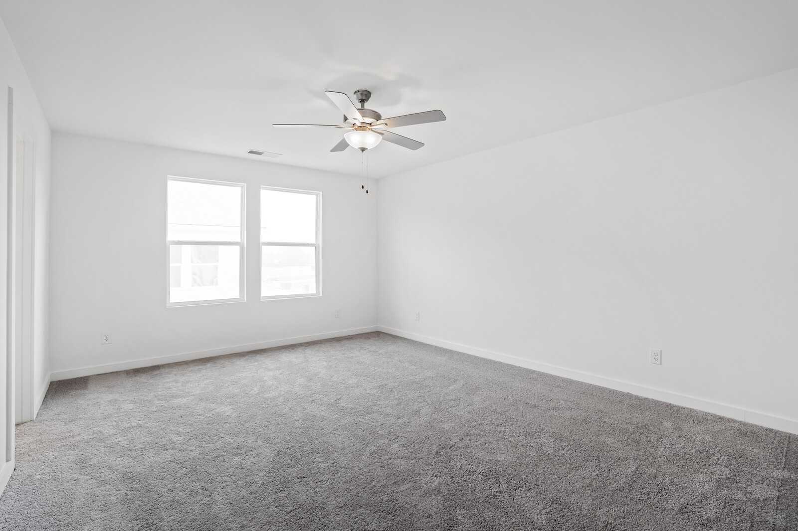 Bright bedroom with gray carpet, white walls, ceiling fan, and double windows in Davidson Homes The Logan B, Calista Farms, White House, TN
