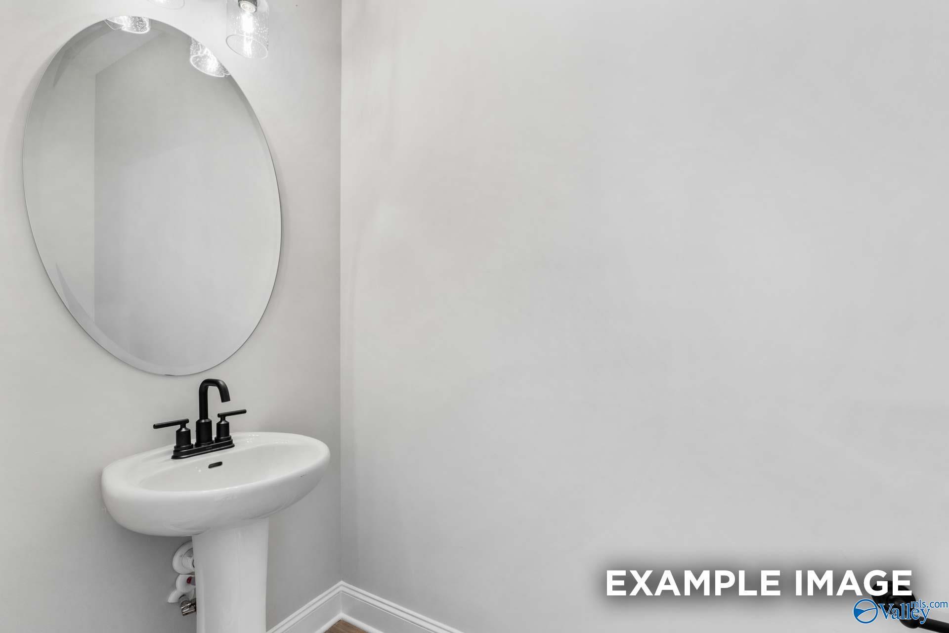 Elegant powder room with round mirror and white pedestal sink in Davidson Homes The Finleigh, Meridianville, Alabama