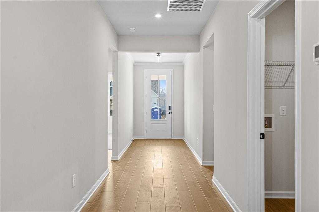 Bright hallway with light hardwood floors, white walls, and open doors in Davidson Homes The Edison A, Loganville, GA
