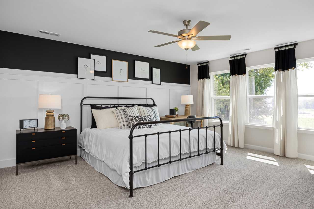 Spacious master bedroom in Wellers Knoll Lillington NC with black metal bed frame, neutral bedding, ceiling fan, and large curtained windows