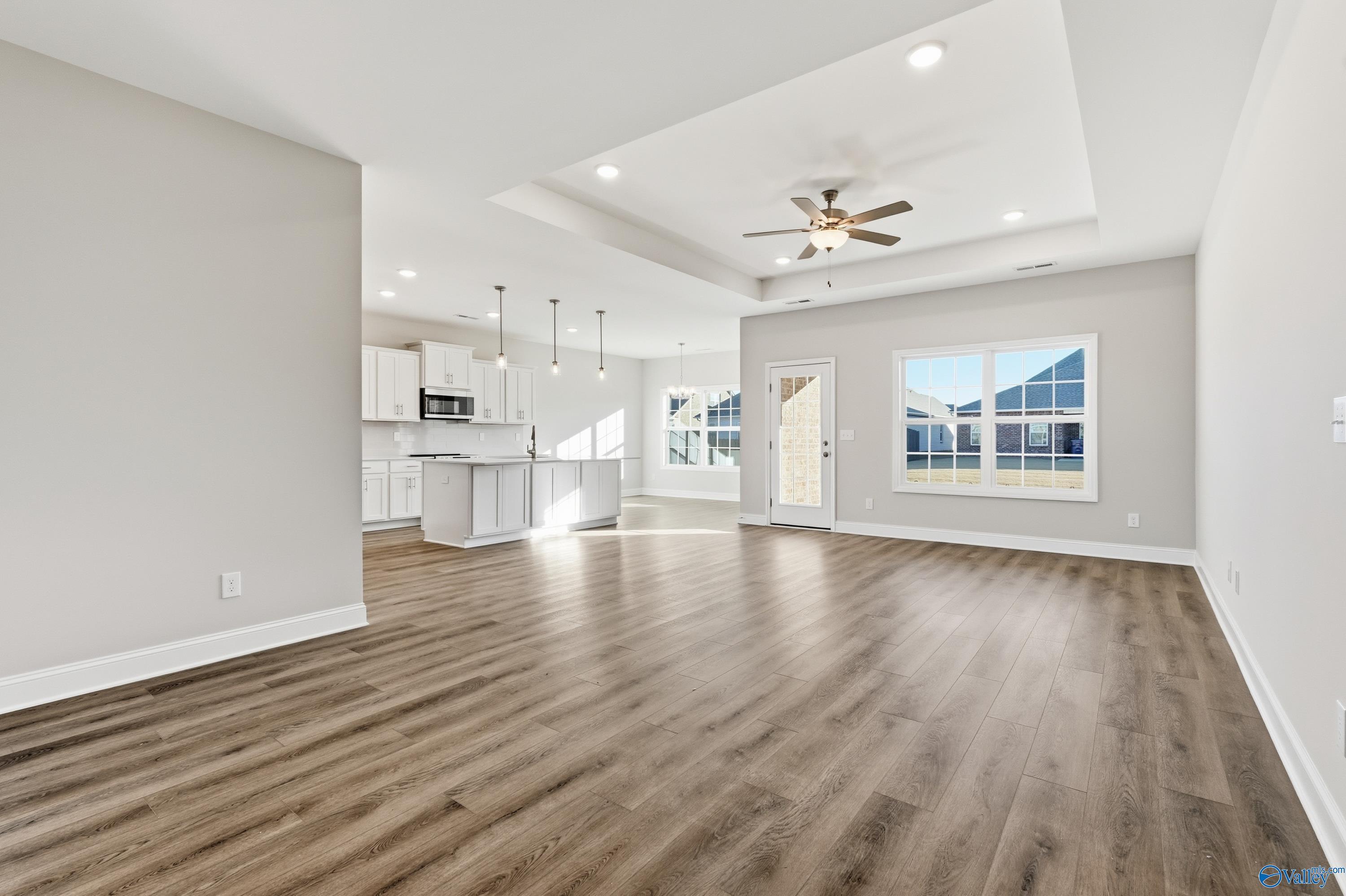 Open-concept living room and kitchen with hardwood floors, white cabinets, island, and ceiling fan in The Montgomery B, Toney, Alabama