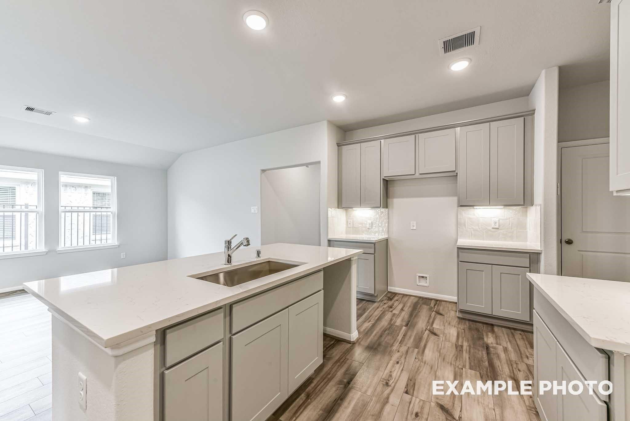 Modern kitchen with quartz island, gray cabinets, and wood-look flooring in The Laguna C floor plan, Sunterra, Katy, TX.