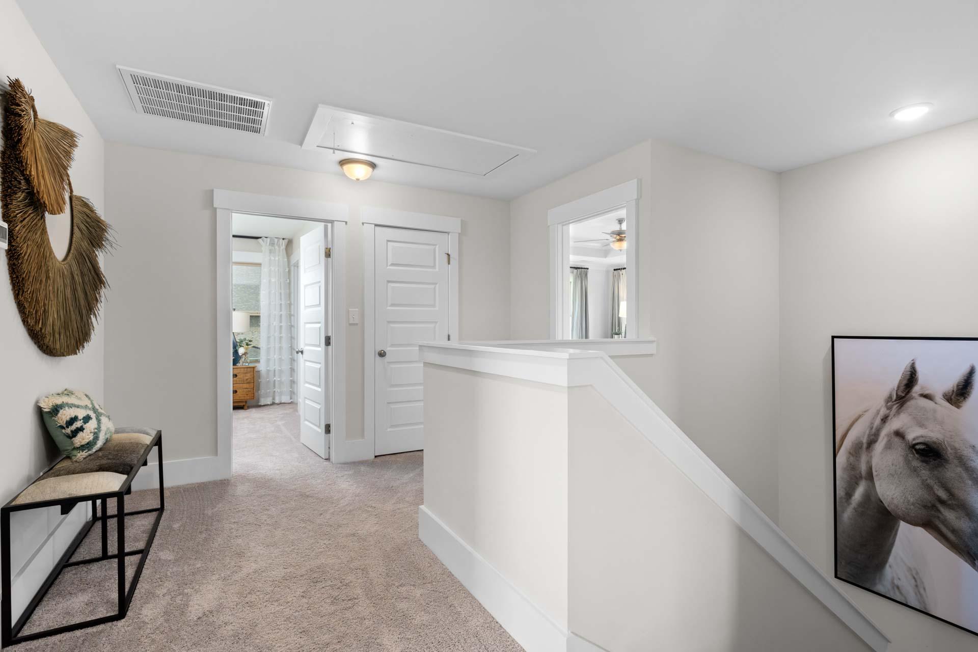 Spacious upstairs hallway at Walker's Hill in Meridianville, Alabama with neutral walls, carpeted floors, white doors, staircase railing, and wall art