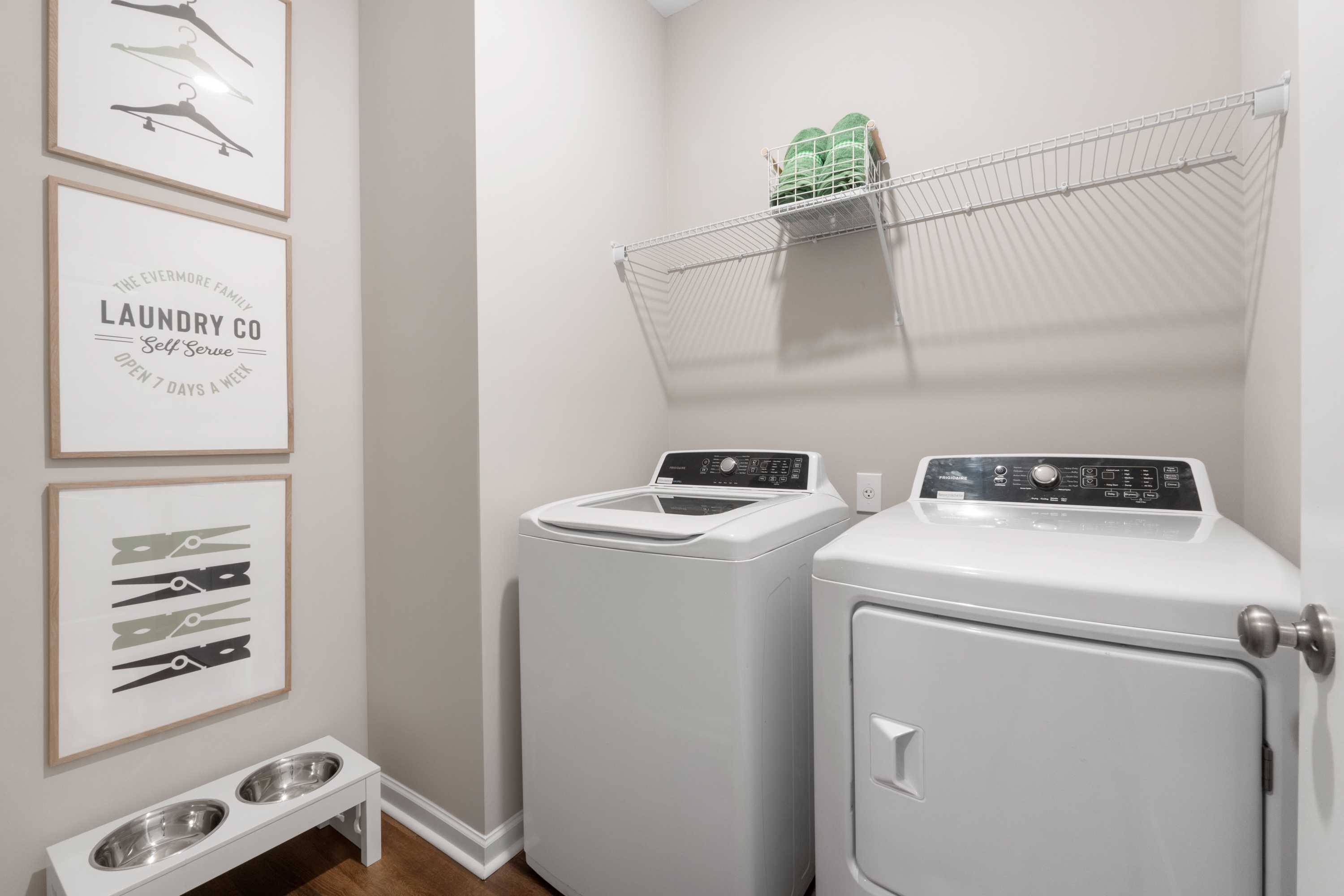 Spacious laundry room at Evergreen Mill in Madison, Alabama with white washer dryer, wall shelving, and decorative art