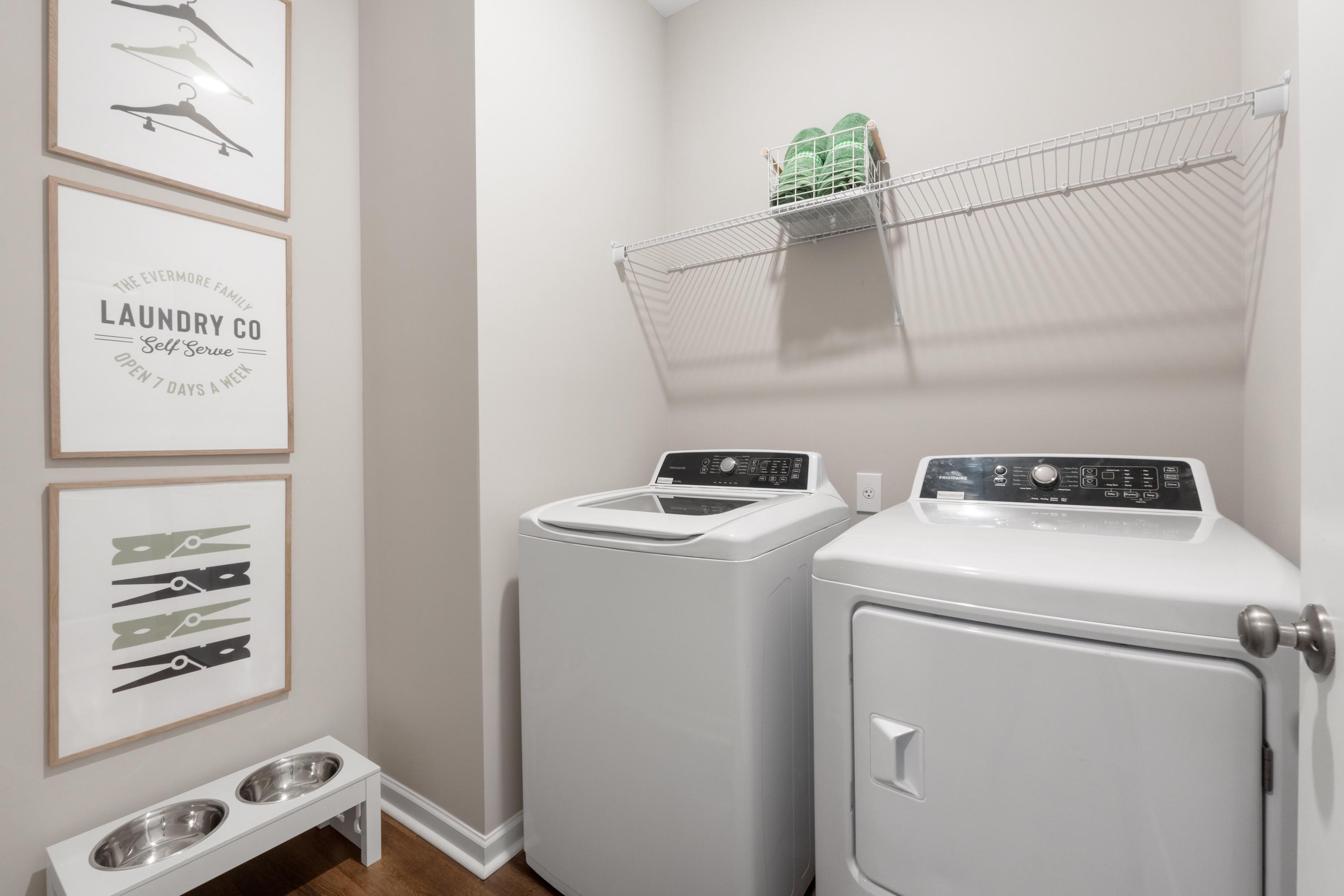 Spacious laundry room at Evergreen Mill in Madison, Alabama with white washer dryer, wall shelving, and decorative art