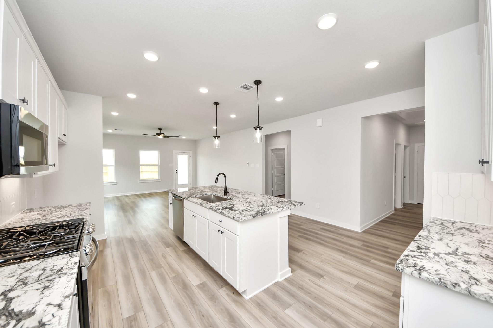 Modern open-concept kitchen with granite island and white cabinetry in The Sorrento E floor plan, Sundance Cove, Crosby.