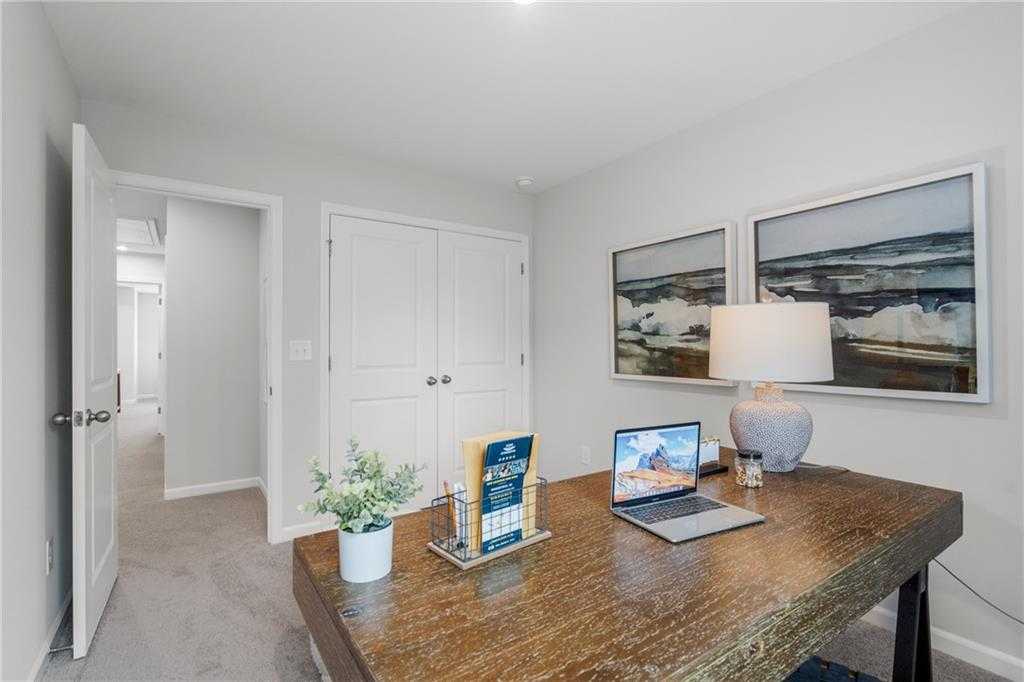 Cozy home office with rustic wooden desk, MacBook laptop, seascape art, and plants in Davidson Homes The Durant A, Emerson, GA