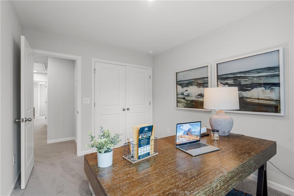 Cozy home office with rustic wood desk, open MacBook, abstract seascape art, potted plant, and closet in Davidson Homes The Durant B, Emerson, GA
