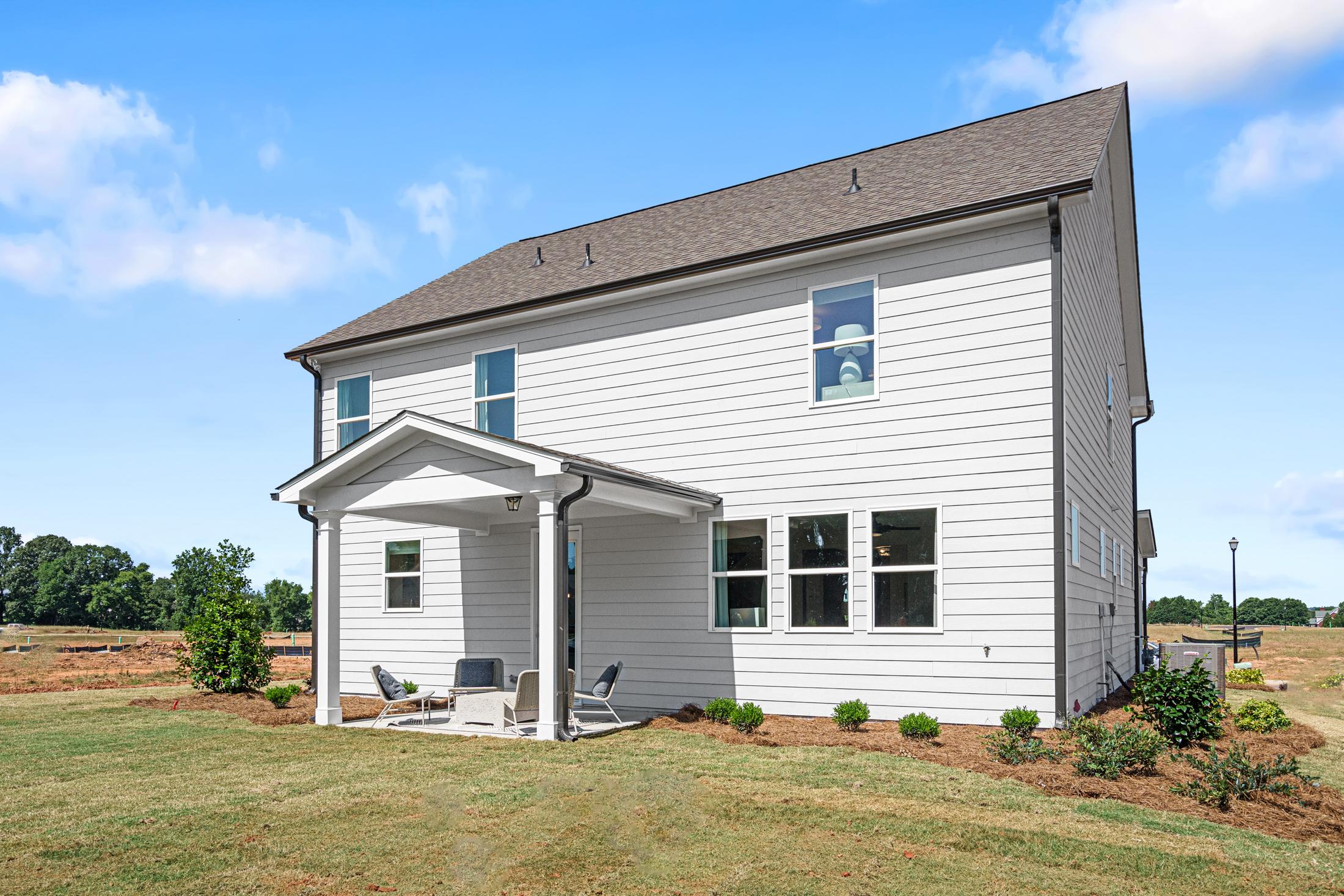 Side view of The Hickory B two-story home with covered porch, white siding, large windows, and patio seating in Hoschton, GA