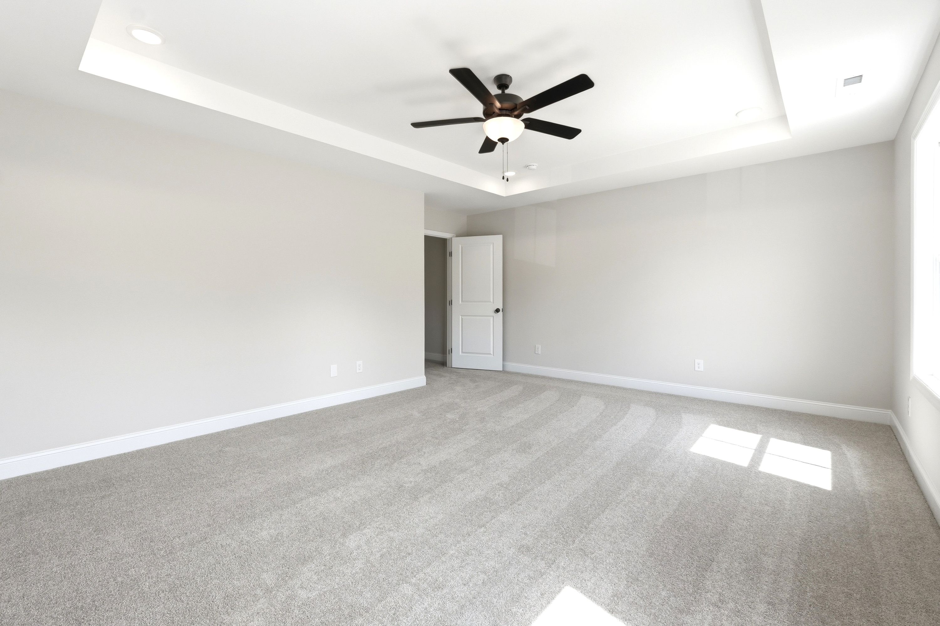 Spacious master suite in The Russell A by Davidson Homes featuring a tray ceiling, ceiling fan, and plush carpet.