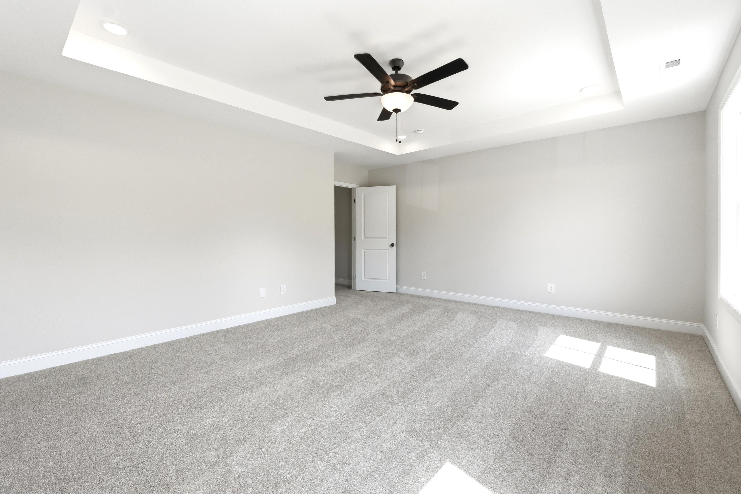 Spacious master suite in The Russell A by Davidson Homes featuring a tray ceiling, ceiling fan, and plush carpet.